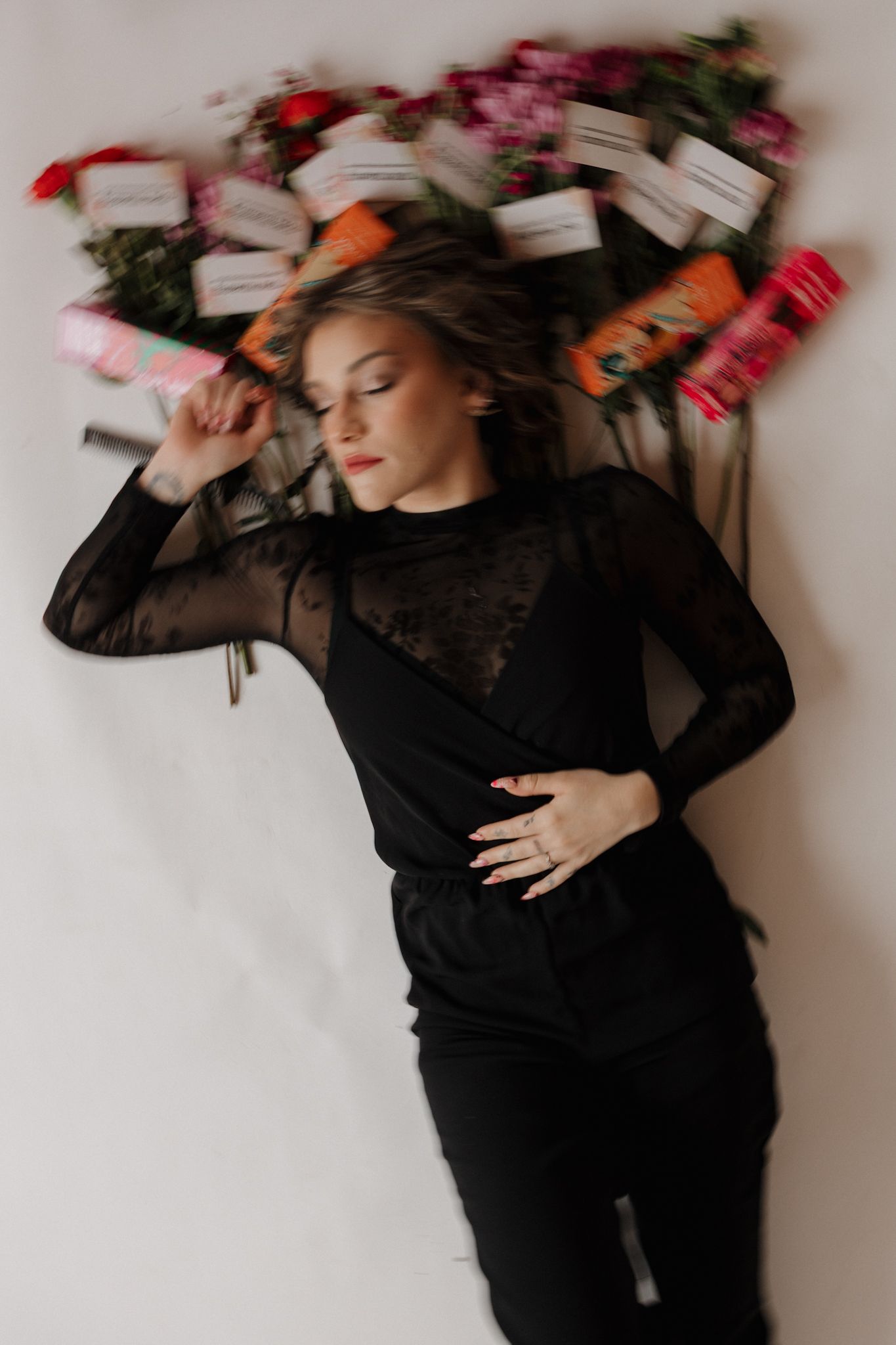 A series of artistic portraits showing a person in black clothing laying on white background with scattered red flowers.