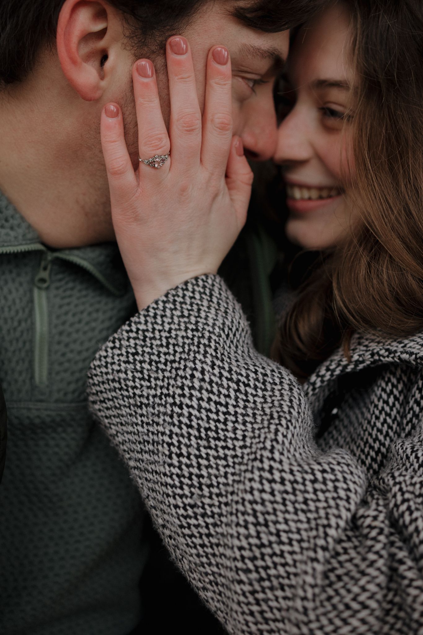Close up romantic moment showing engagement ring on hand while couple embraces wearing cozy winter sweaters.