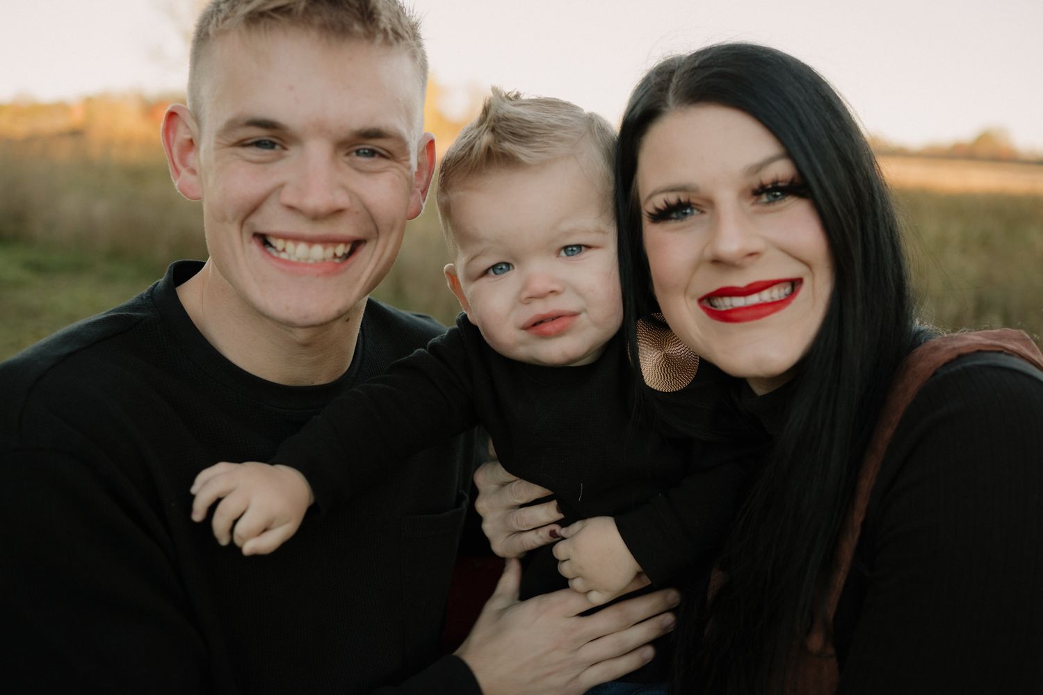 A family poses together in an outdoor setting during golden hour with a warm sunset glow in the background.