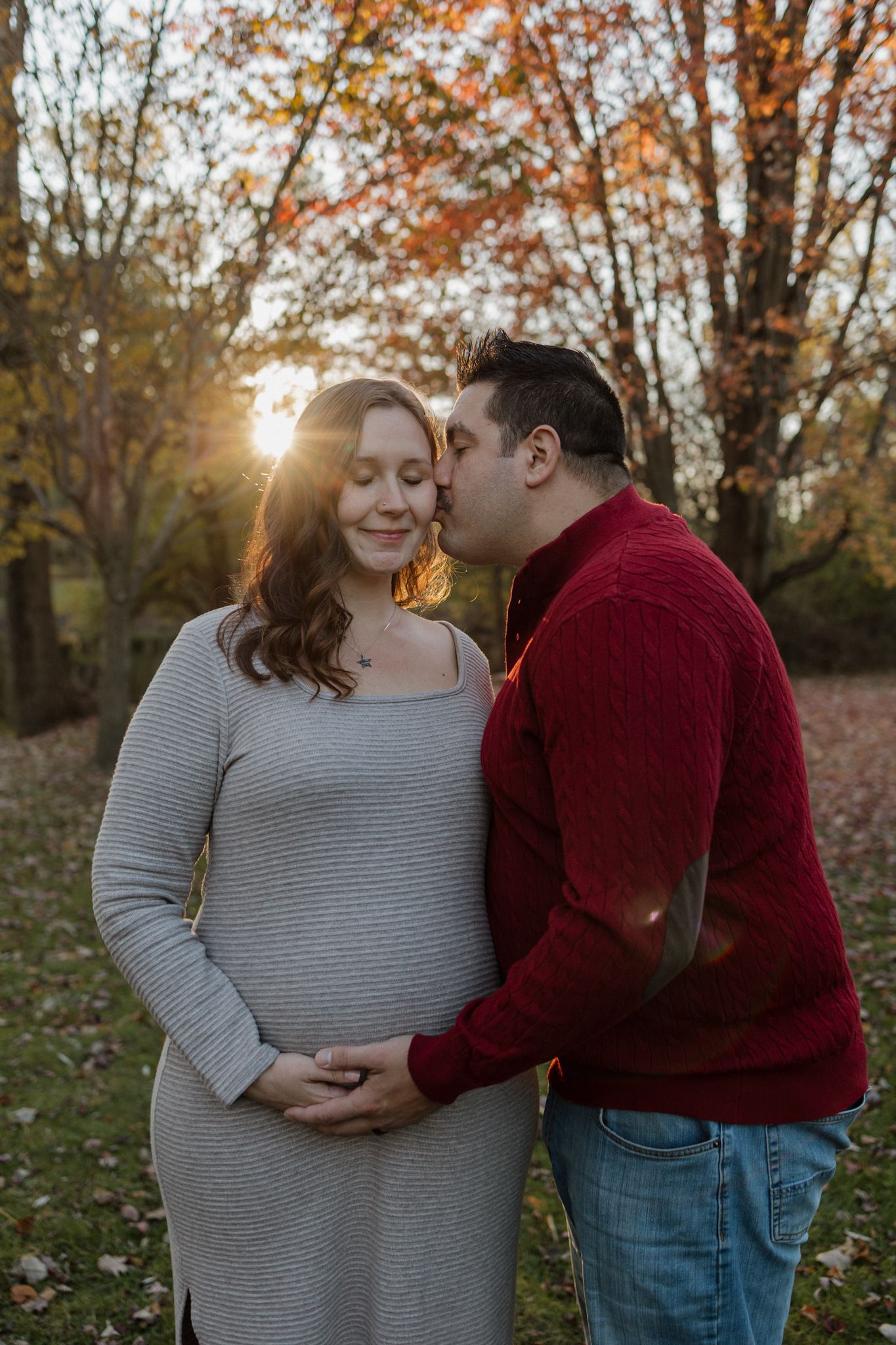 A couple shares tender moments in an autumn setting with golden sunlight filtering through fall foliage.