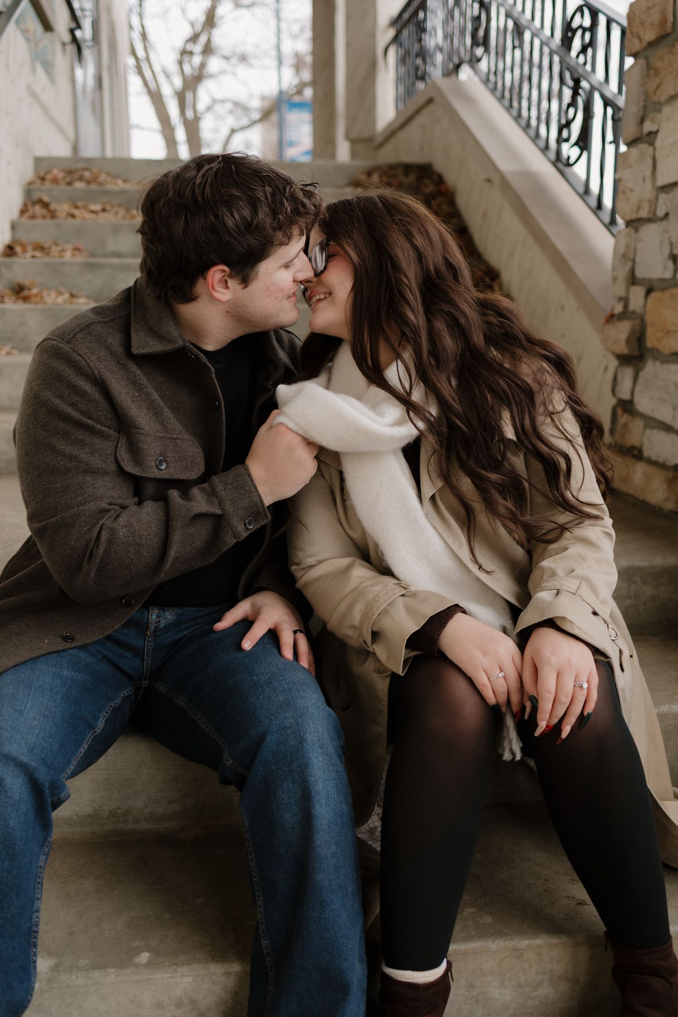 A romantic couple shares intimate kisses while sitting together on wooden stairs in a vintage-style setting.