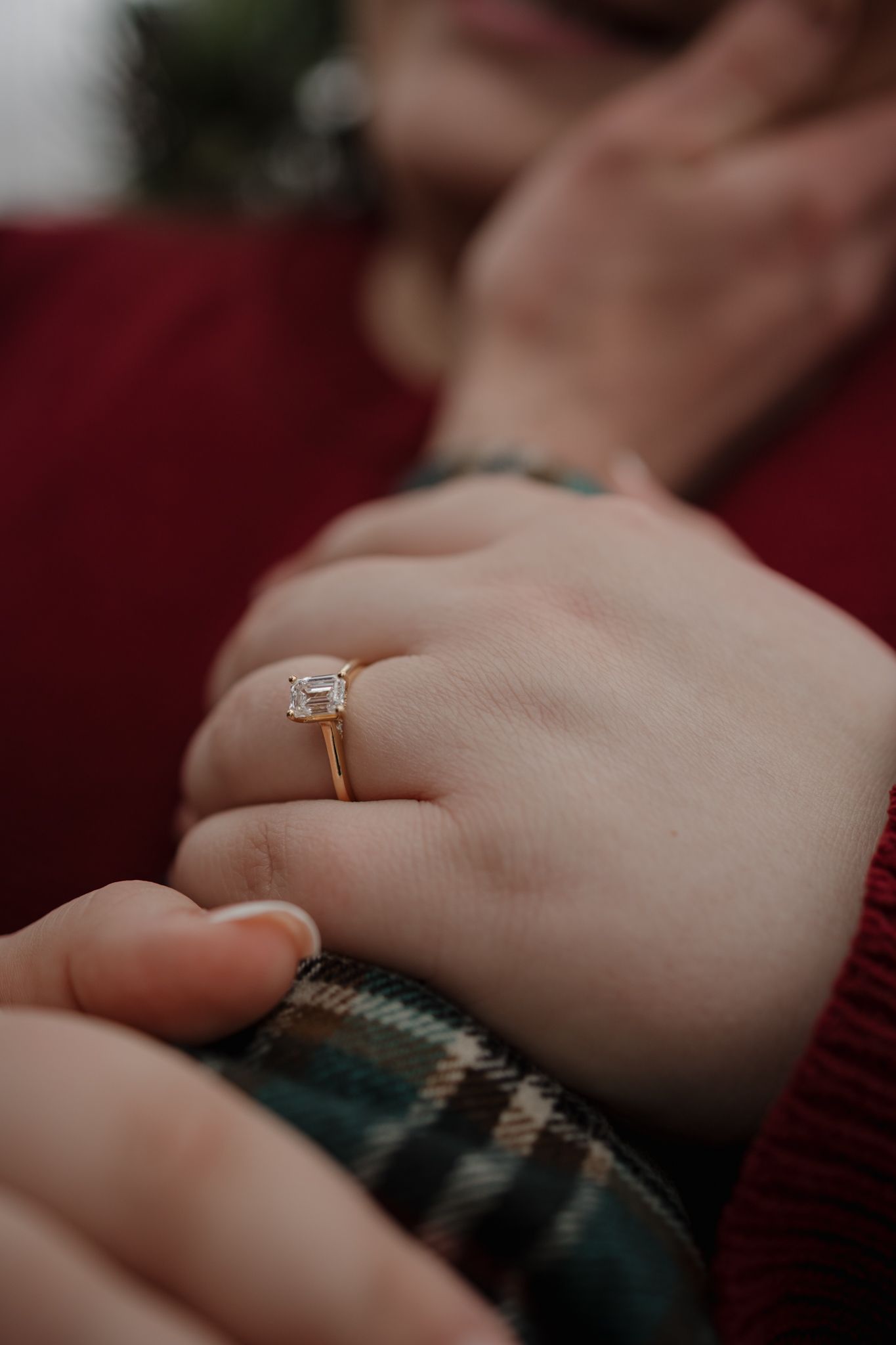 Close-up view of hands wearing engagement rings resting on a cozy knit sweater in warm lighting.