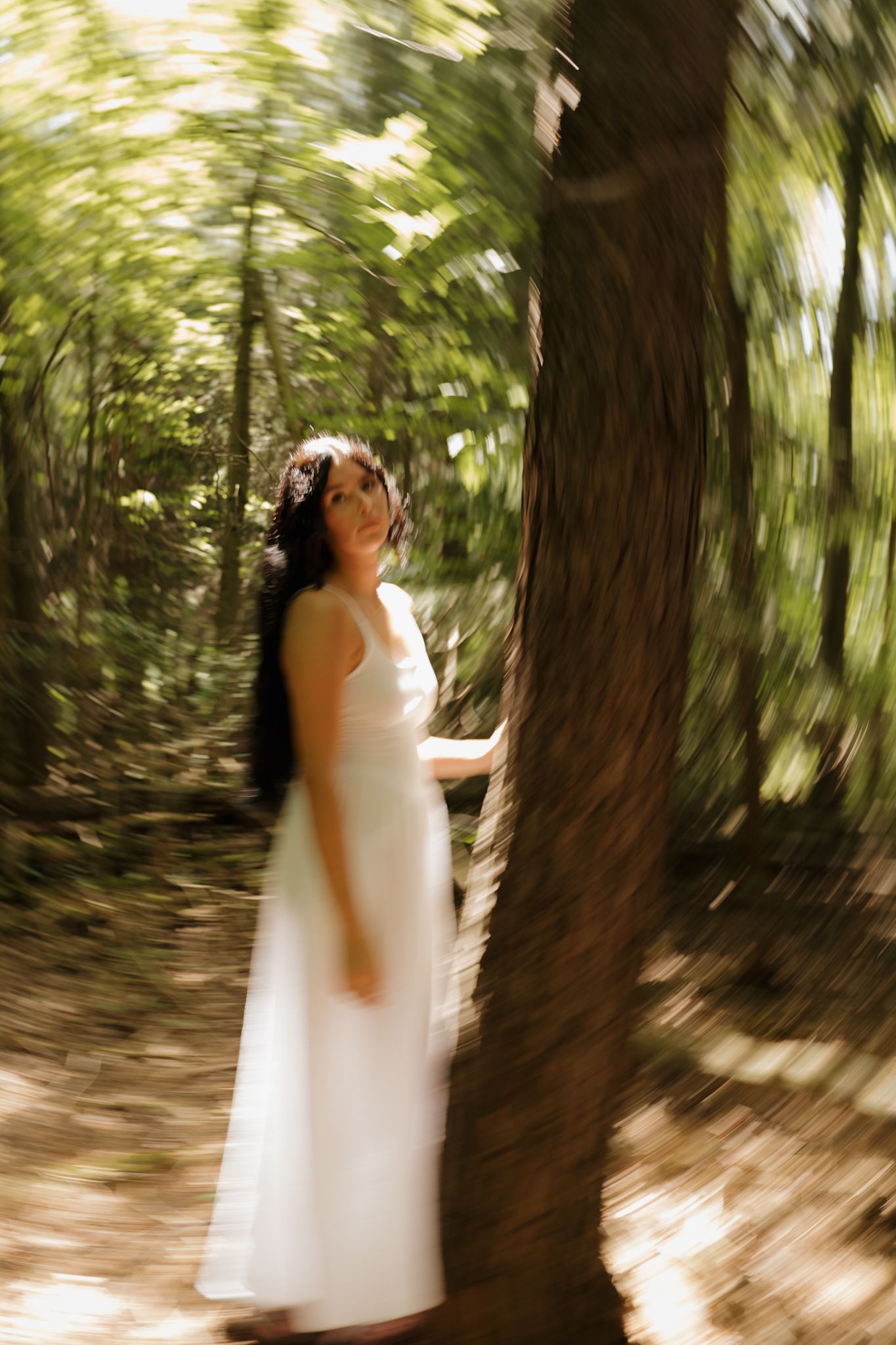Motion-blurred sequence of a person in a white dress walking through a sunlit forest path.
