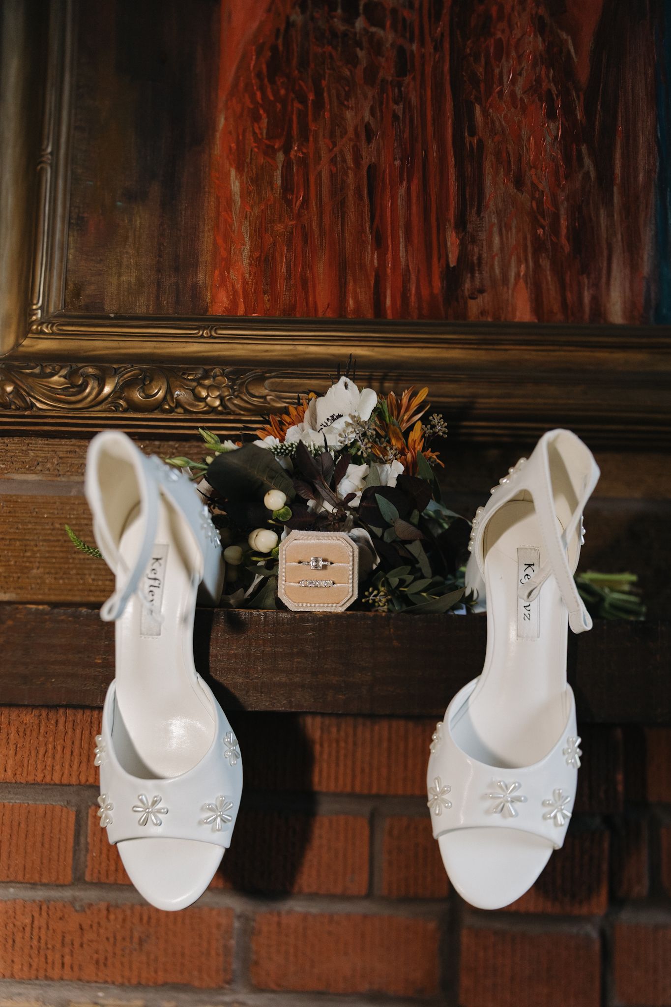 A row of elegant white bridal shoes displayed on a wooden mantel with floral decorations.
