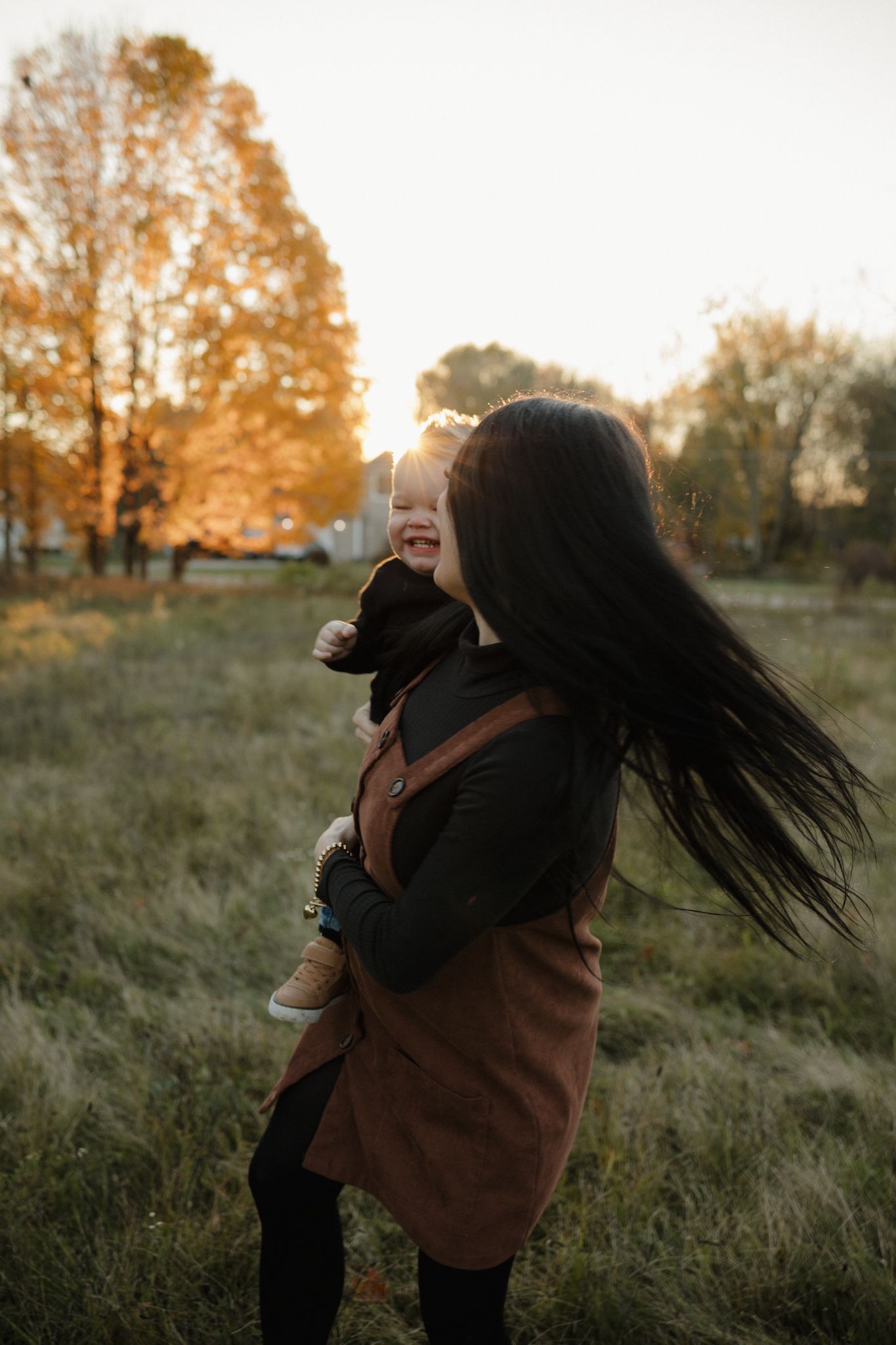 A couple embraces in a golden autumn field at sunset as long dark hair flows in the wind.