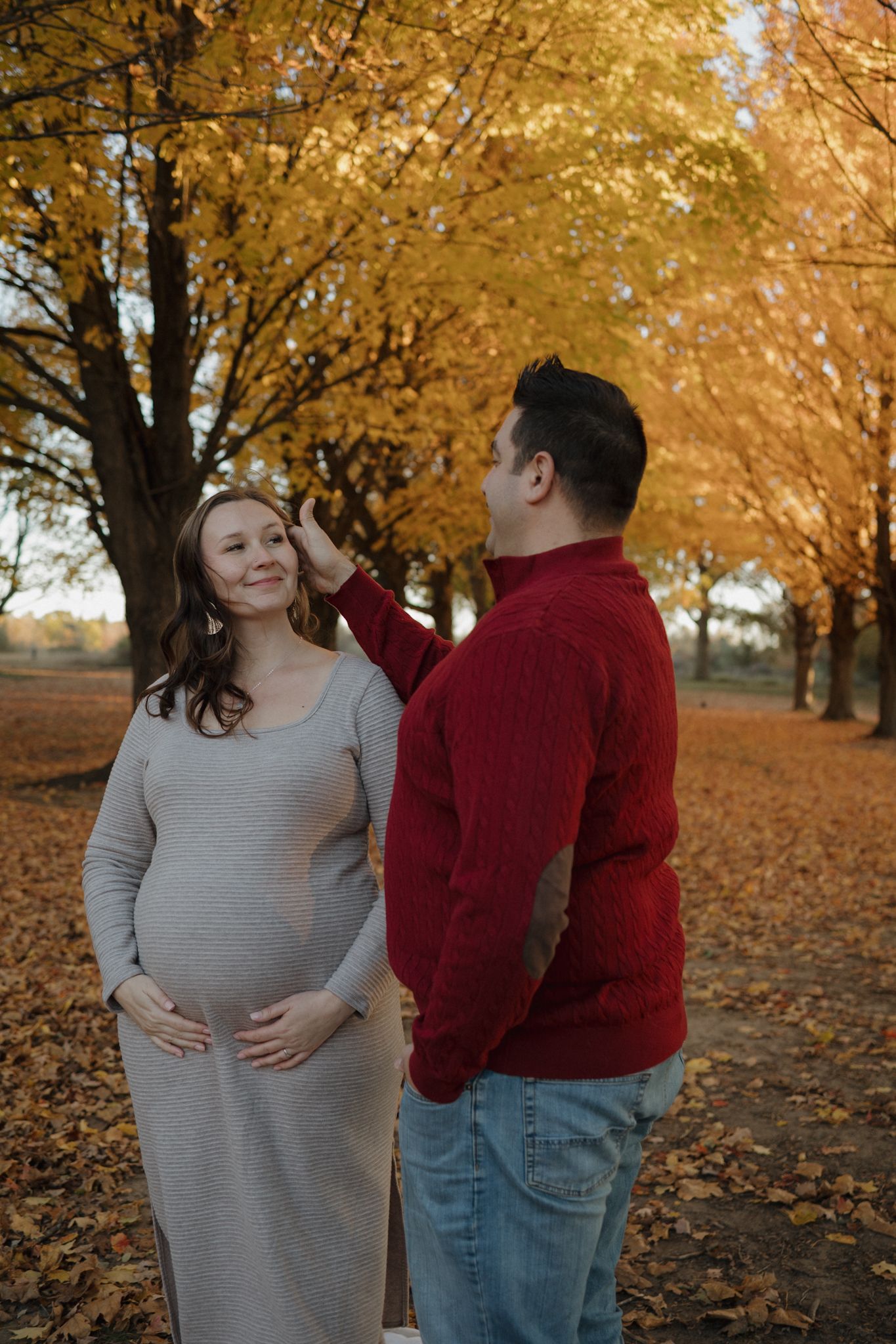 Pregnant couple in autumn park, man tenderly touching woman's hair among golden fall foliage.