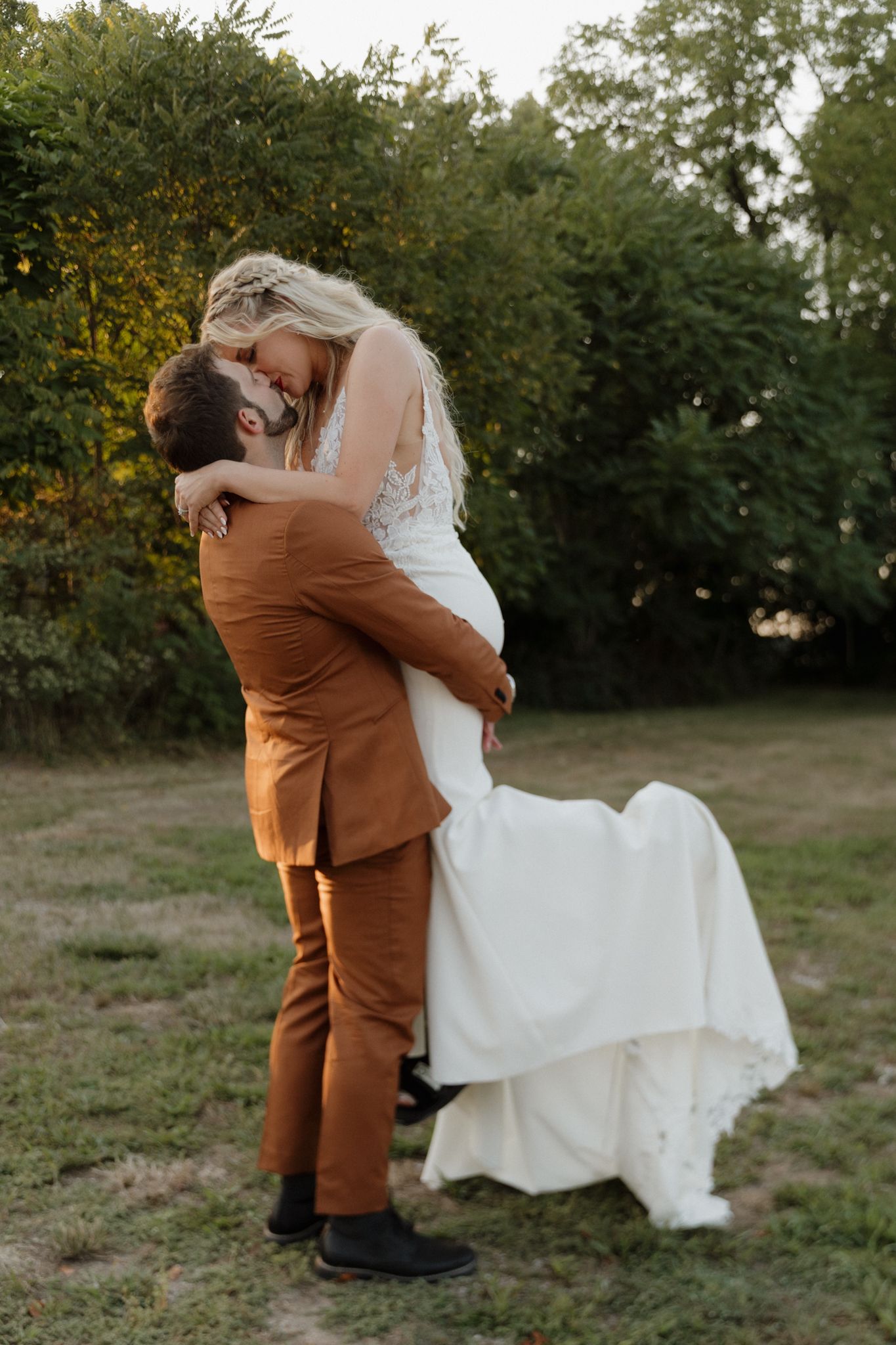 A couple dancing and embracing in a grassy outdoor field at sunset.