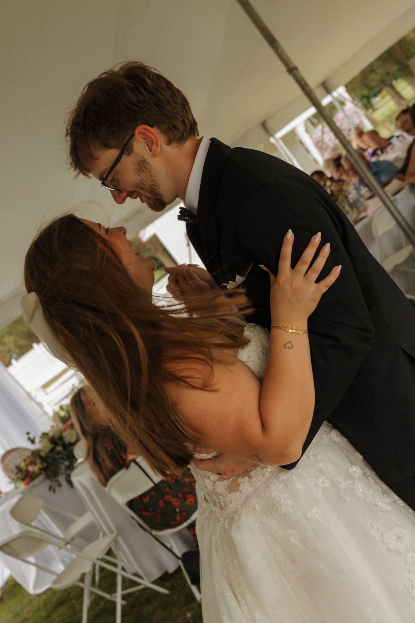Bride and groom share a romantic first dance under a white tent at their outdoor wedding reception.