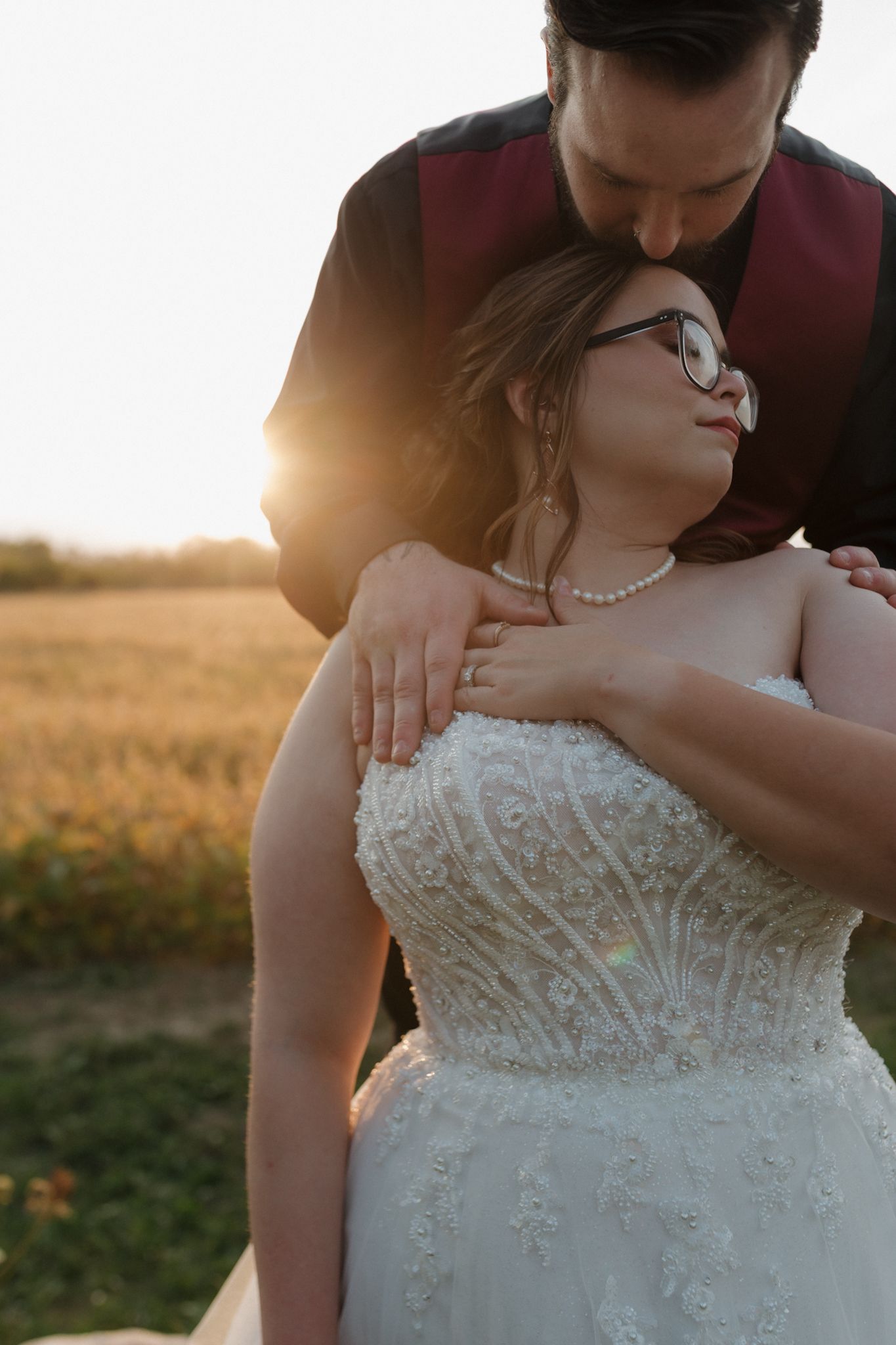 A couple embraces during sunset in a field, with the bride wearing an intricately beaded white wedding dress.