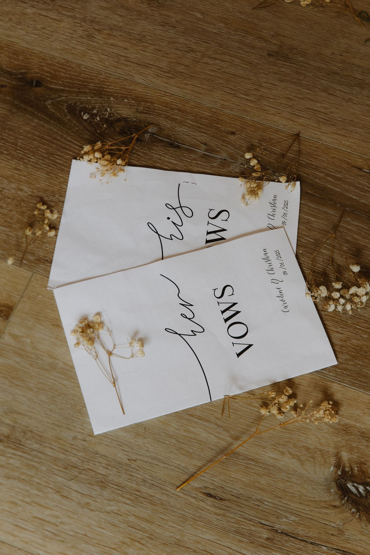 White paper place cards with elegant calligraphy scattered on a wooden surface with dried flowers.