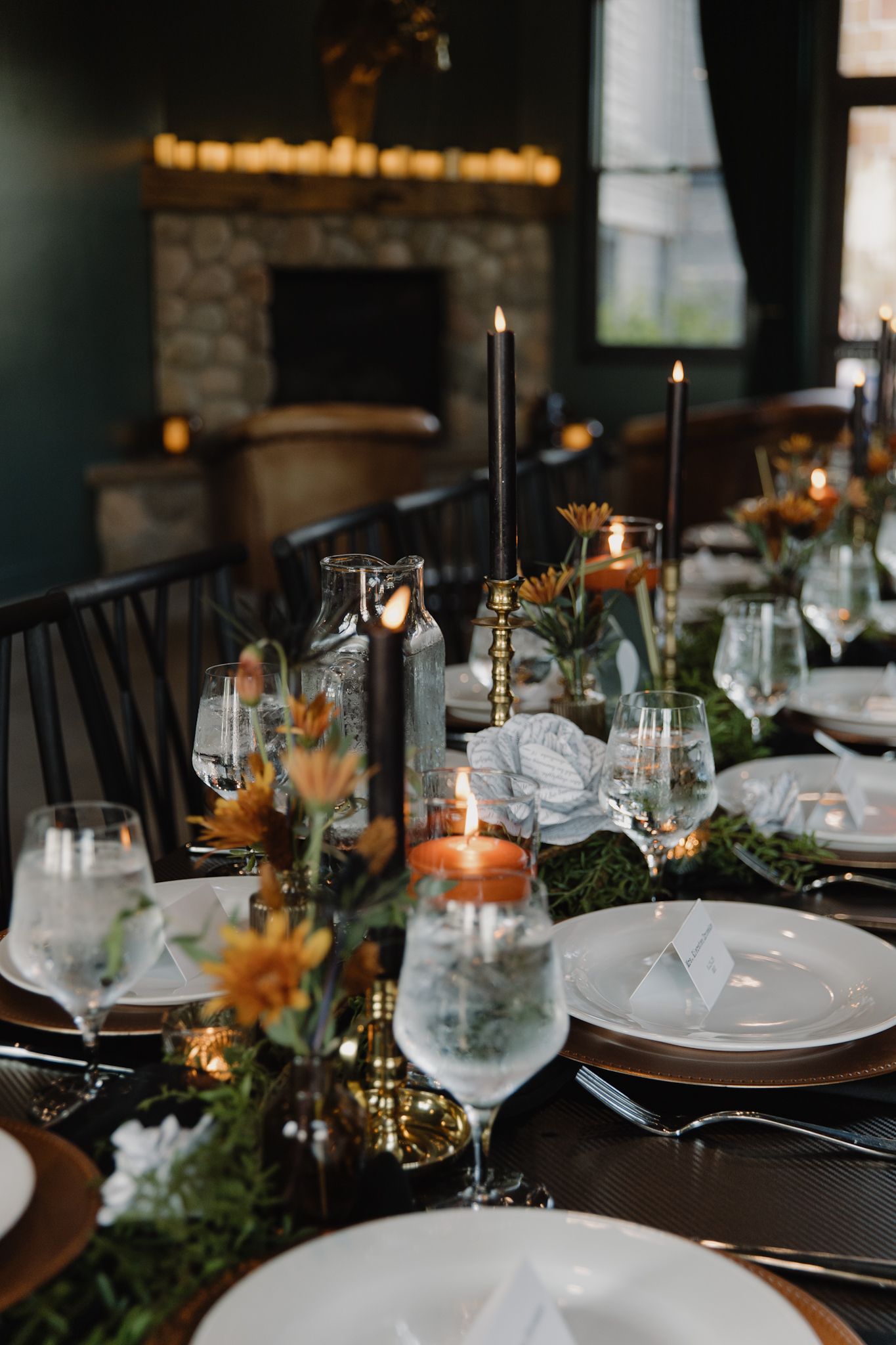 Elegant table setting with black candles, greenery garland, and orange flowers for an intimate dinner party.