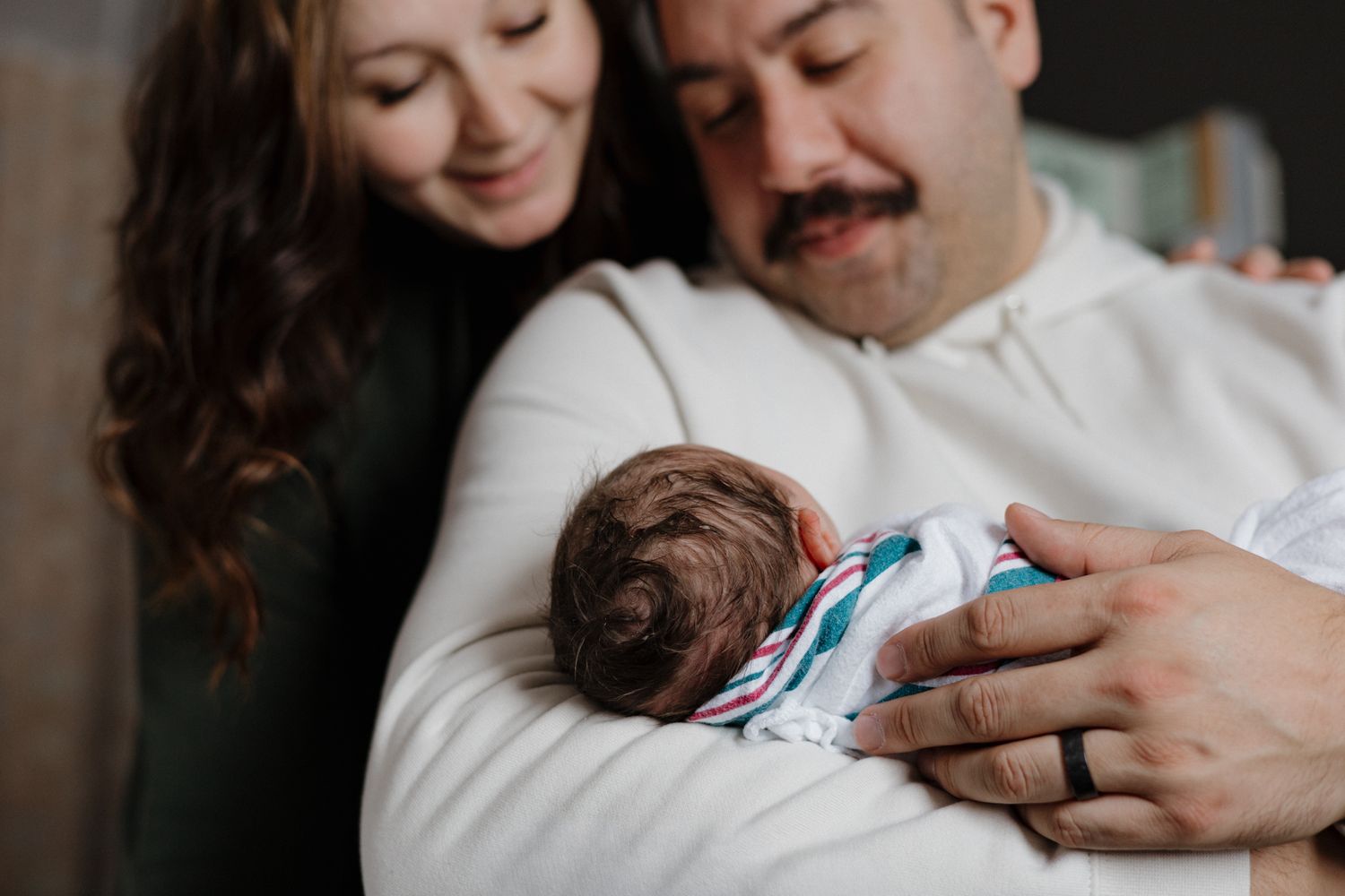 A couple smiles lovingly at their newborn baby wrapped in a striped blanket.
