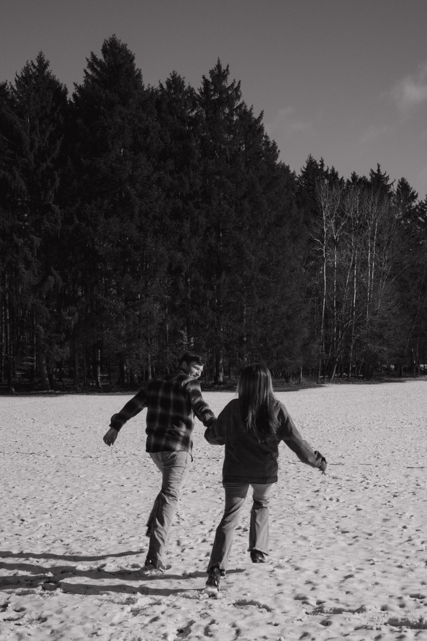 Two people play in deep snow with evergreen trees in the background on a winter day.