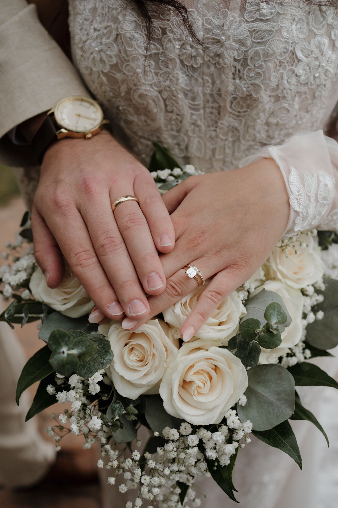 Close-up series of wedding hands with diamond ring against white roses and baby's breath floral arrangement.