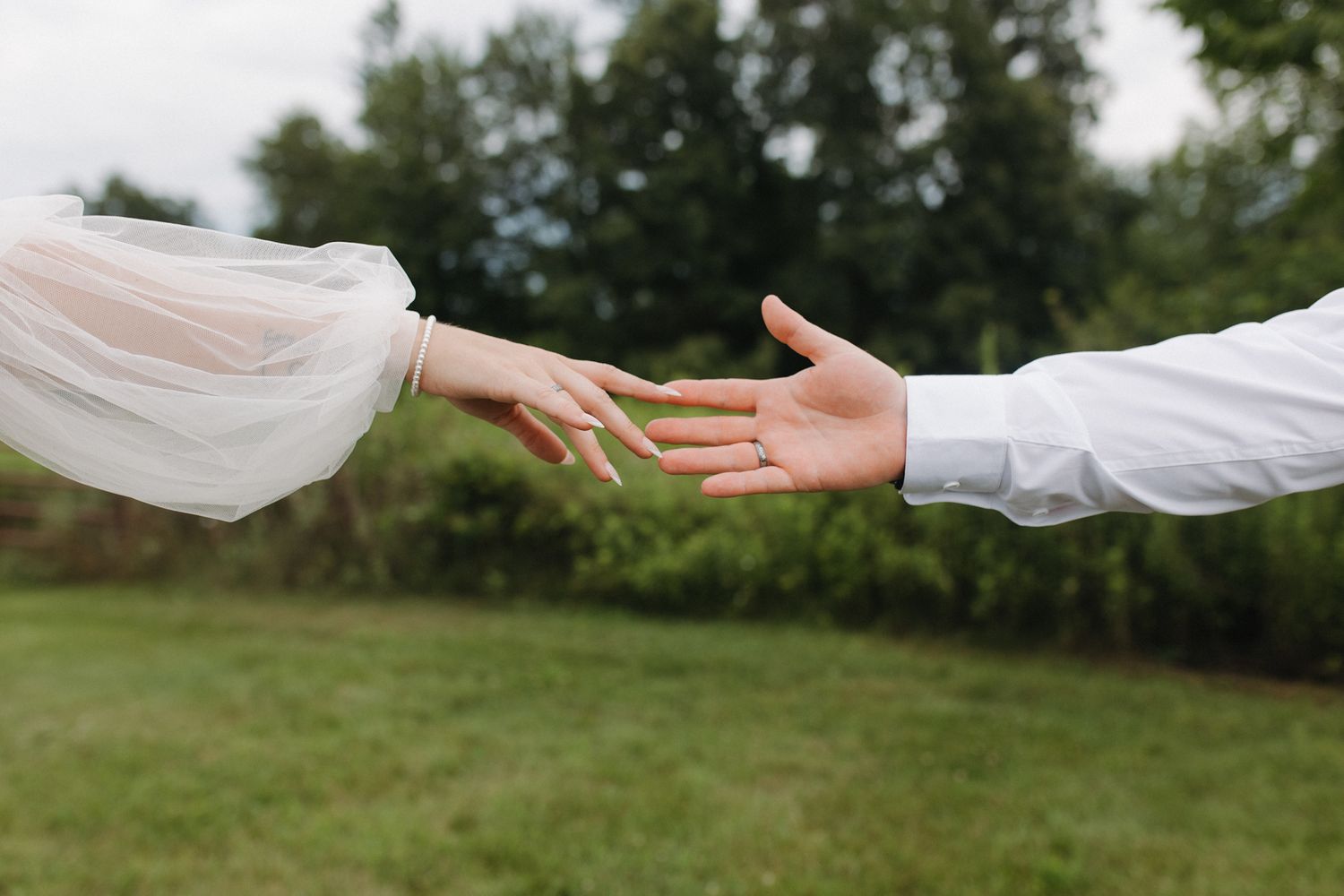 Hands reach toward each other against a bright outdoor background, creating a romantic moment.