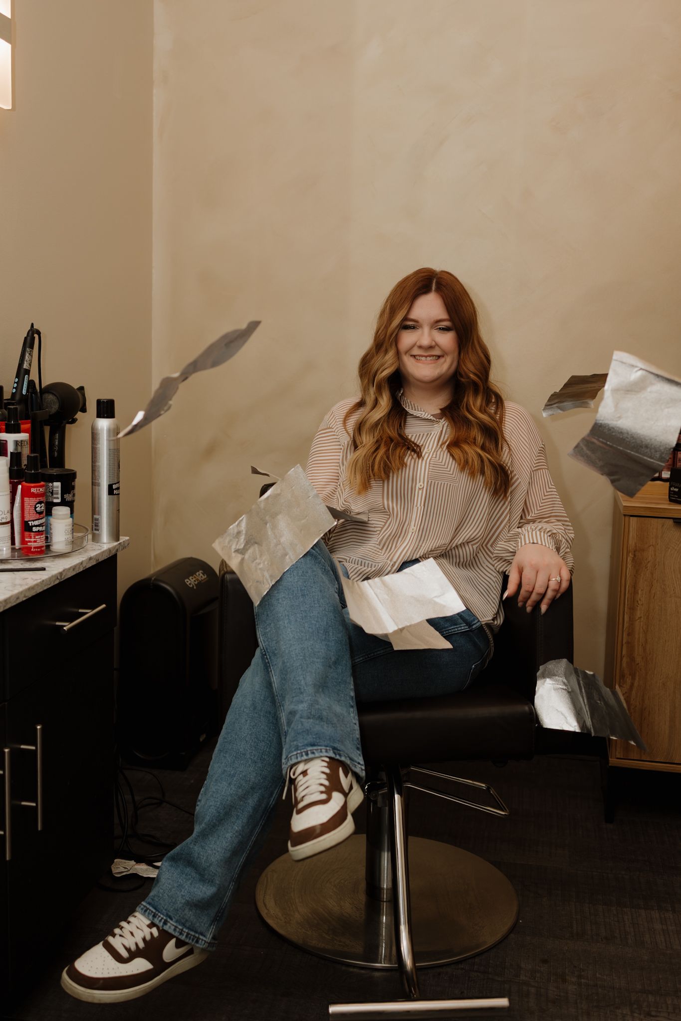 Person in blue jeans and sneakers sits casually in a chair while reading in a dimly lit room.