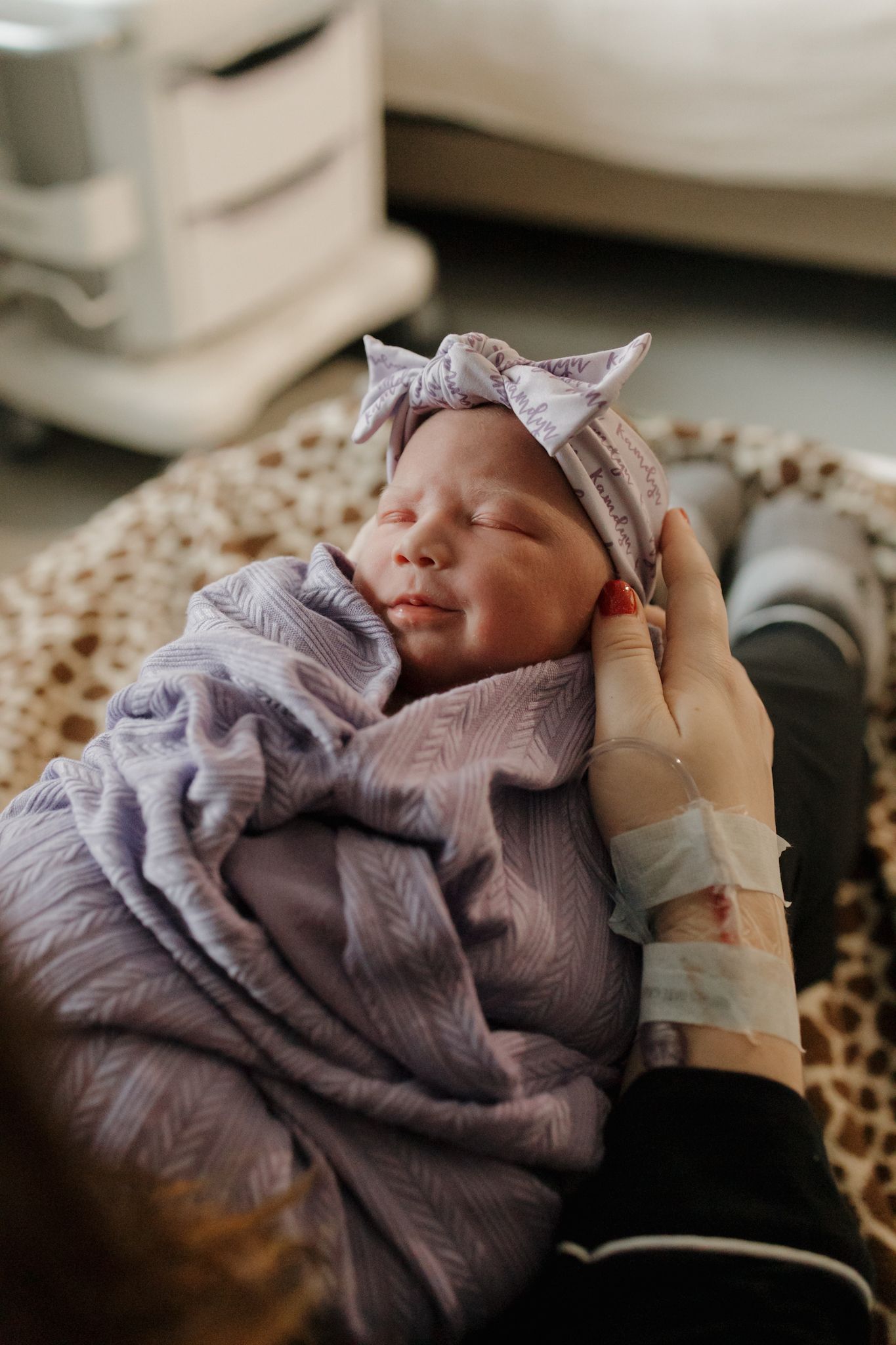 A sleeping infant wrapped in a soft purple blanket with medical monitoring equipment visible.