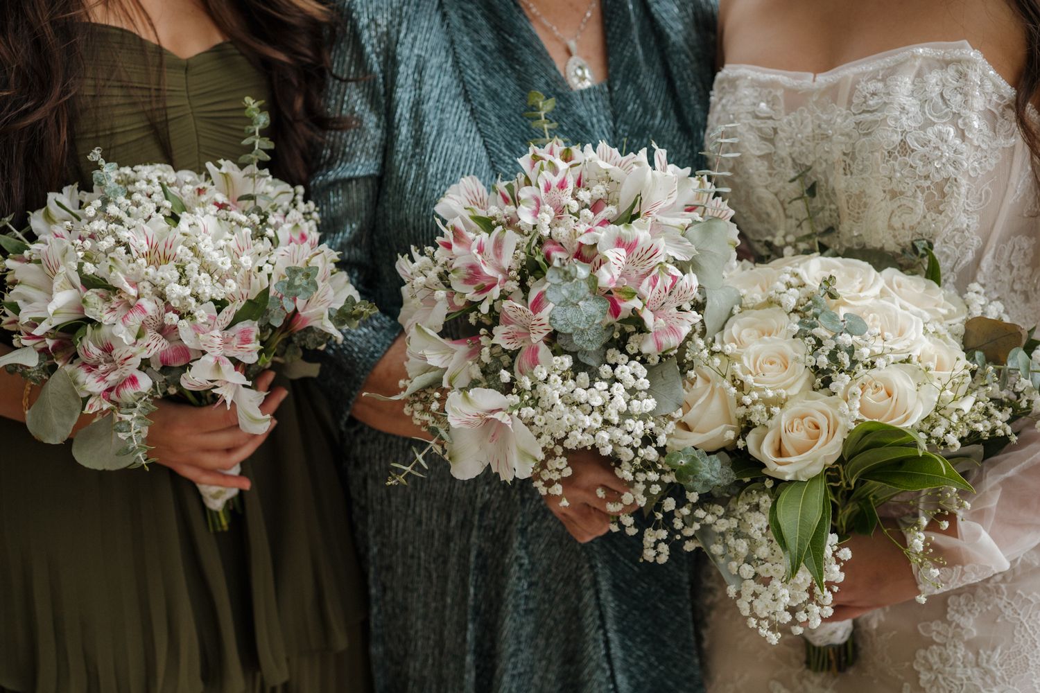 Wedding party holds coordinated bouquets featuring pink and white flowers with delicate baby's breath accents.