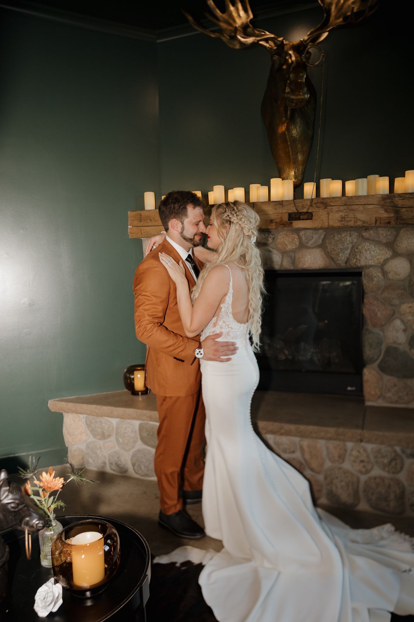 A couple shares an intimate moment in formal attire against a stone fireplace backdrop.