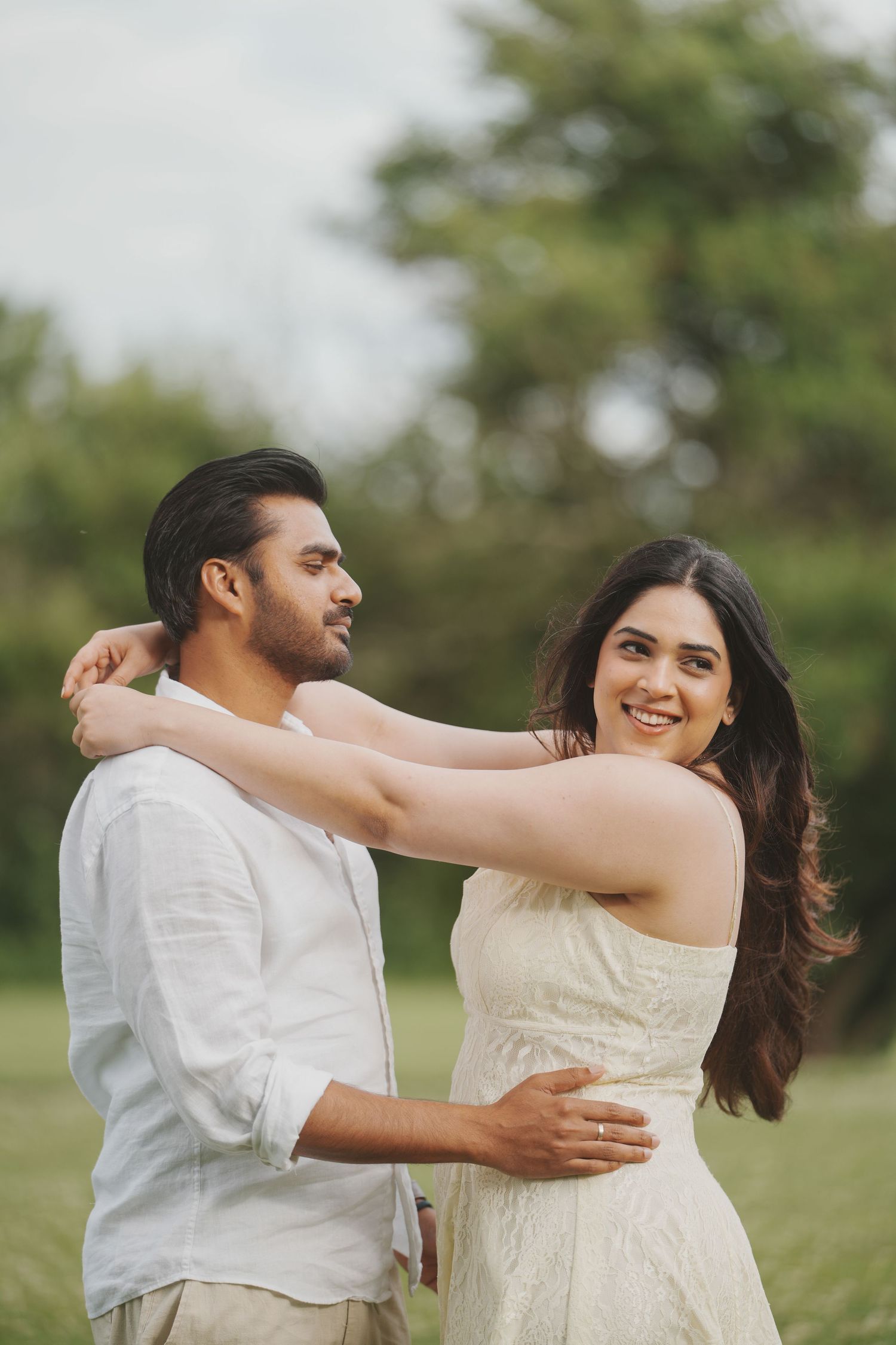 Romantic outdoor portrait of a smiling couple embracing in natural light during an engagement session.