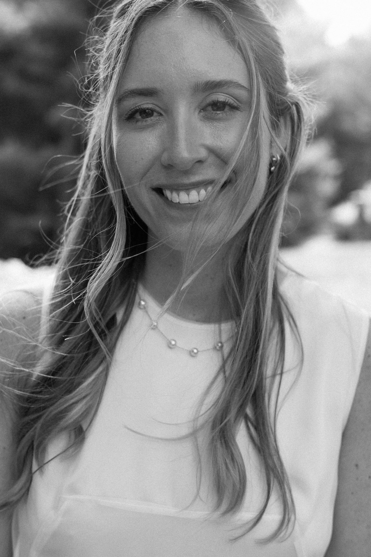 Beautiful bride smiling in black and white close-up portrait wearing pearl necklace outdoors.
