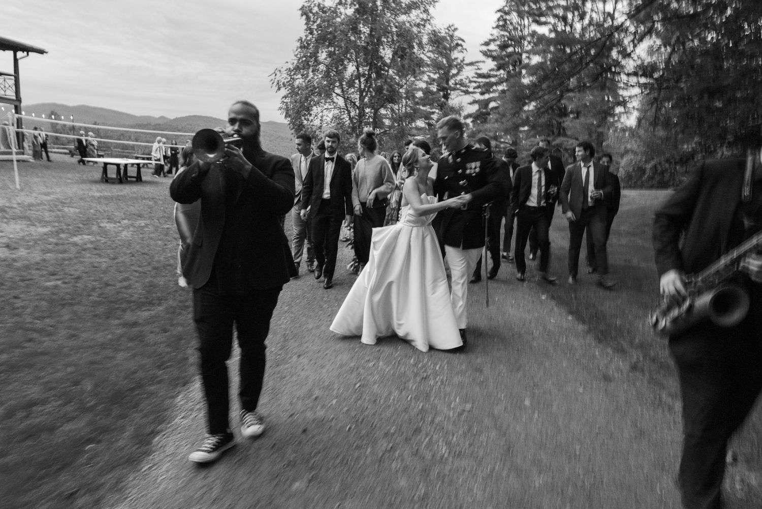 Black and white wedding processional with bride in white gown, groom in military uniform, and jazz musicians leading the way.