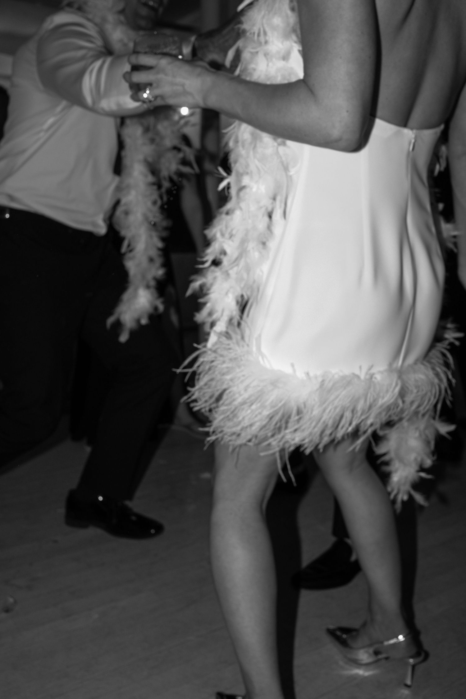 Woman in feathered white flapper dress dancing at elegant wedding reception in black and white photo.