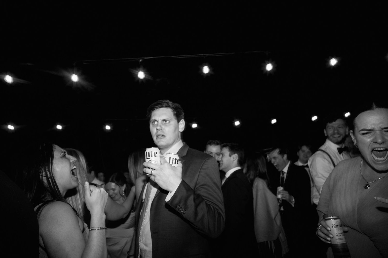 Man holding beer cup at lively wedding reception party with guests.