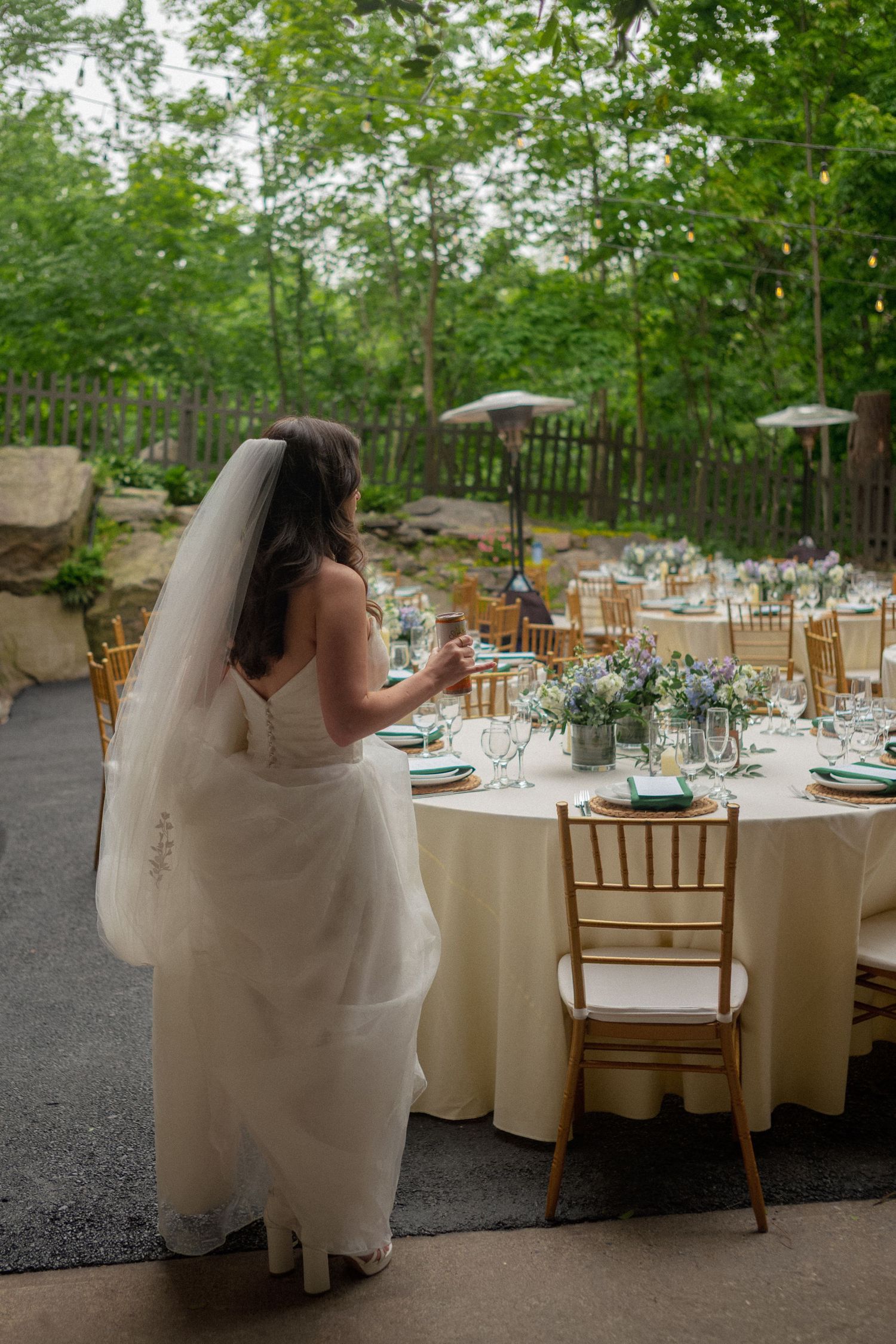 Bride in white gown and veil standing at elegantly set outdoor wedding reception table.