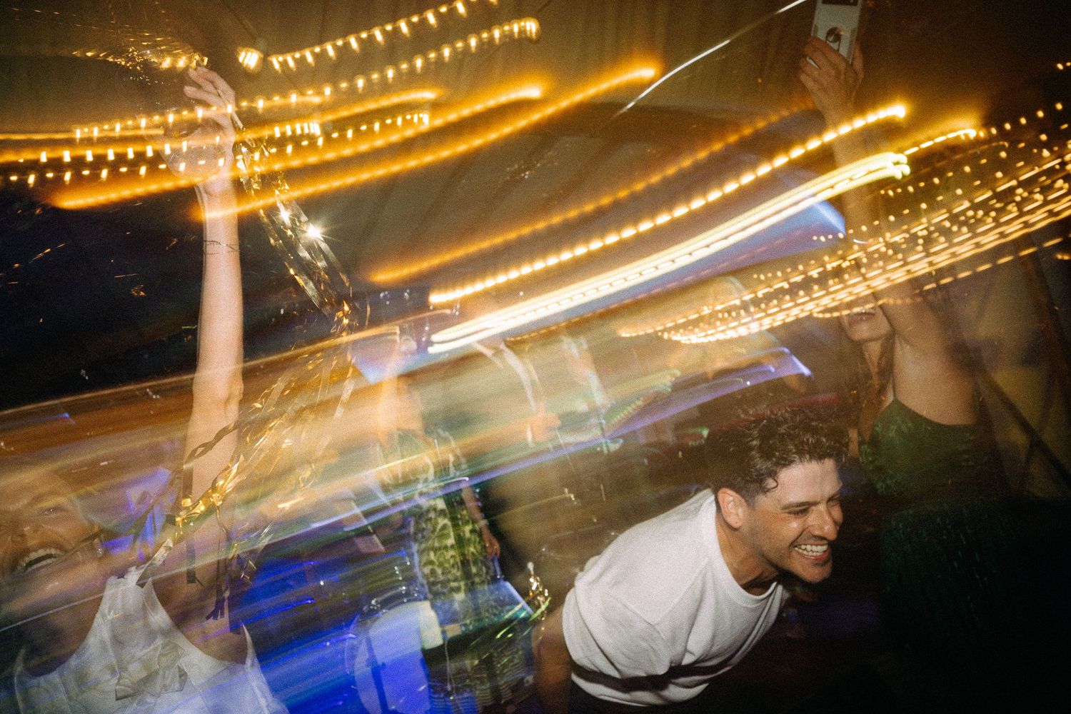 People dancing at a nightclub with colorful light trails and bokeh effects creating a vibrant, energetic atmosphere.