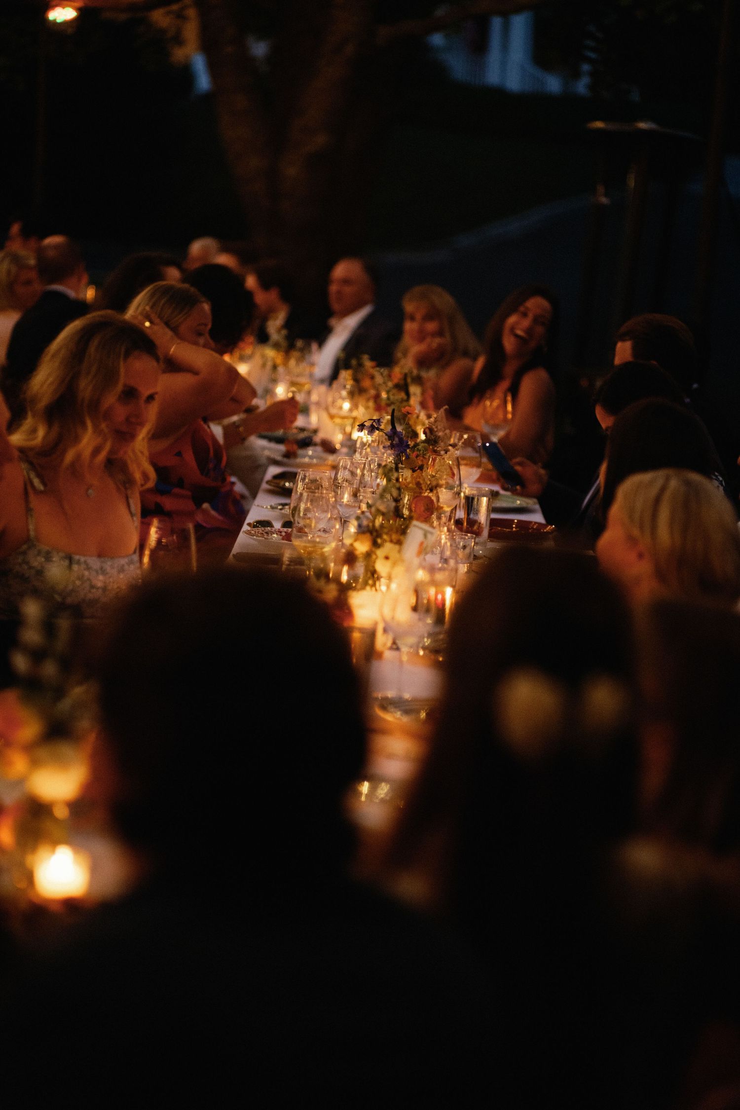 Guests enjoying a romantic candlelit outdoor wedding reception dinner under string lights at night.