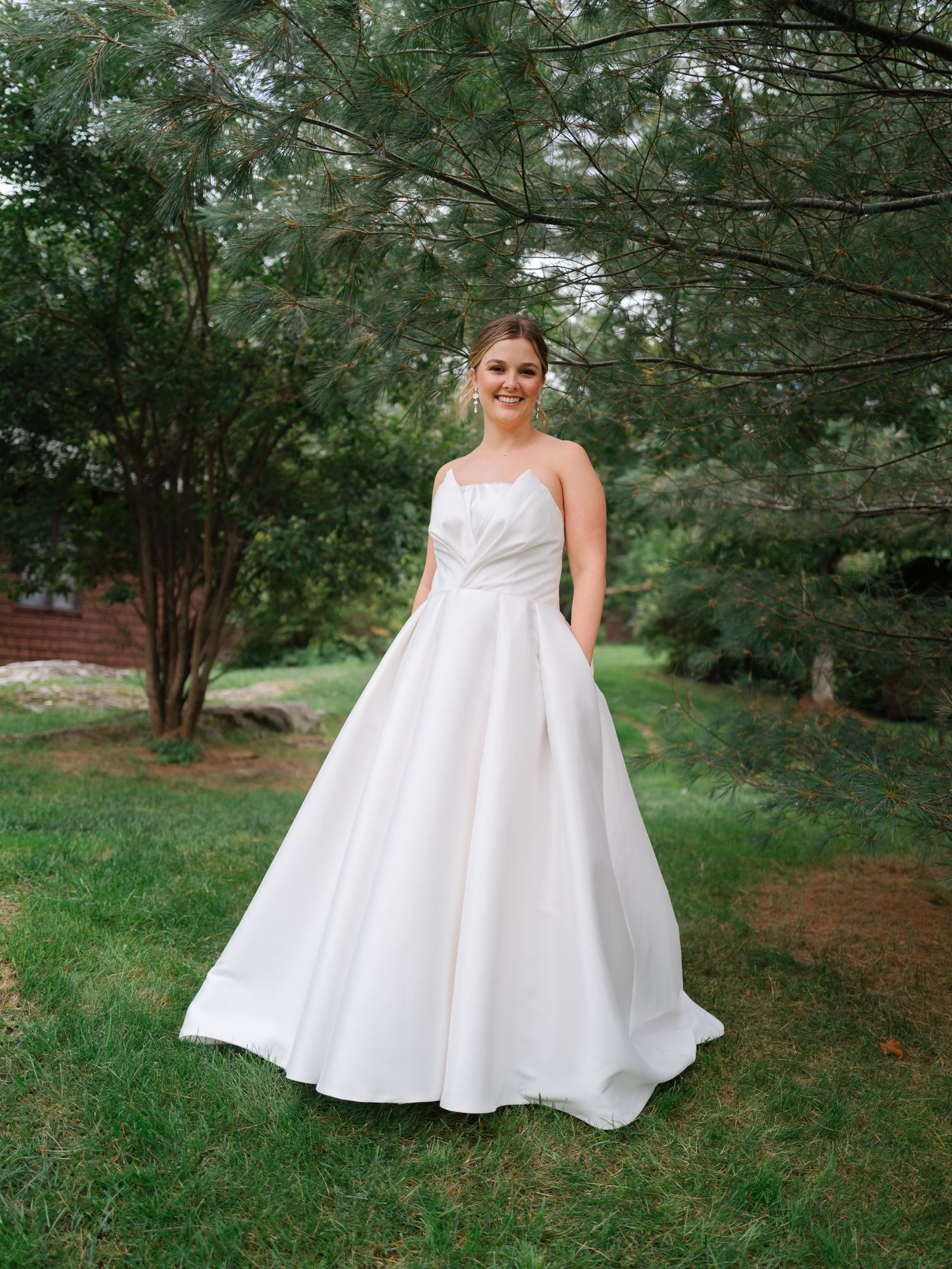 Smiling bride in white ball gown standing in lush garden.