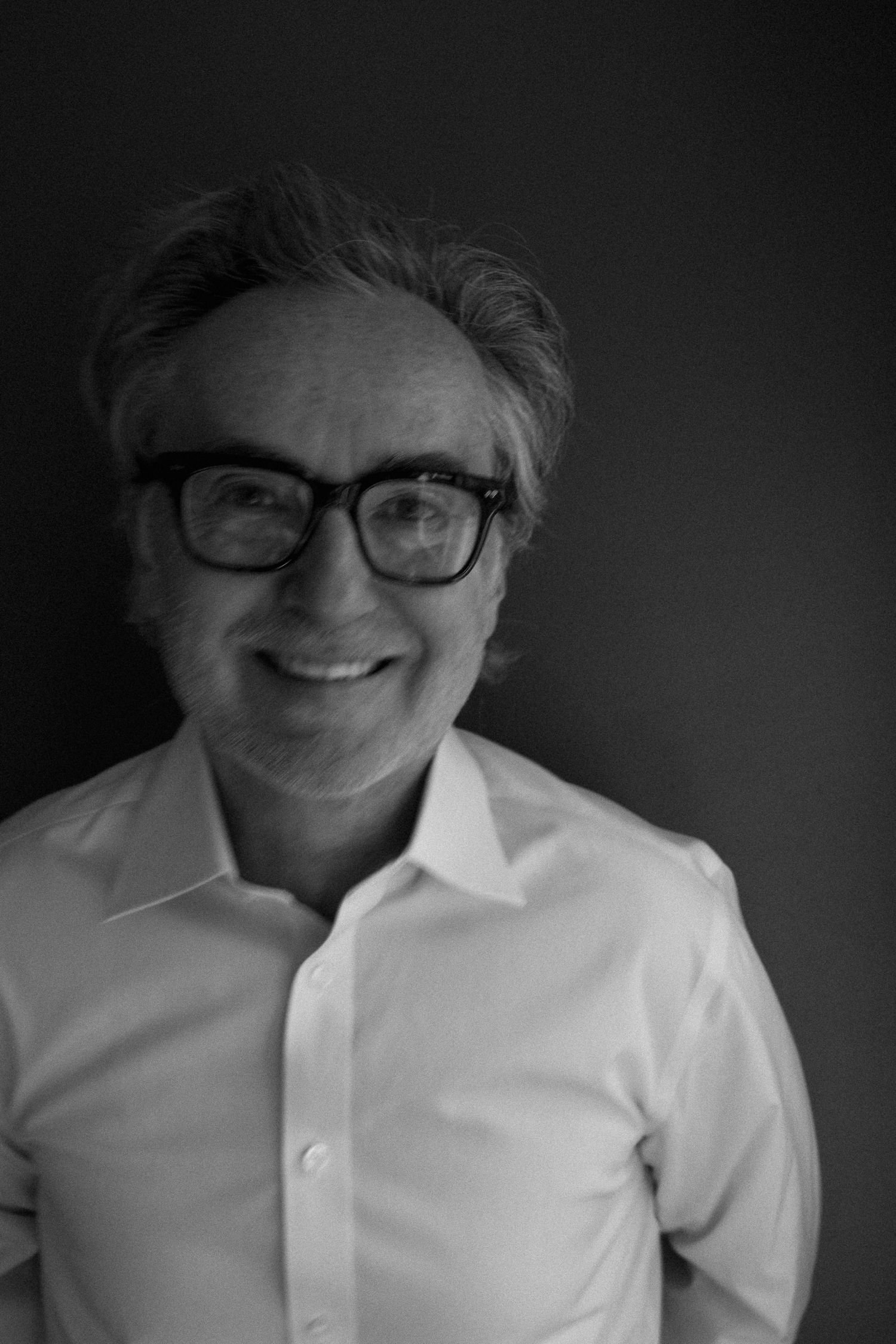 Black and white portrait of a smiling middle-aged man wearing glasses and a white dress shirt.