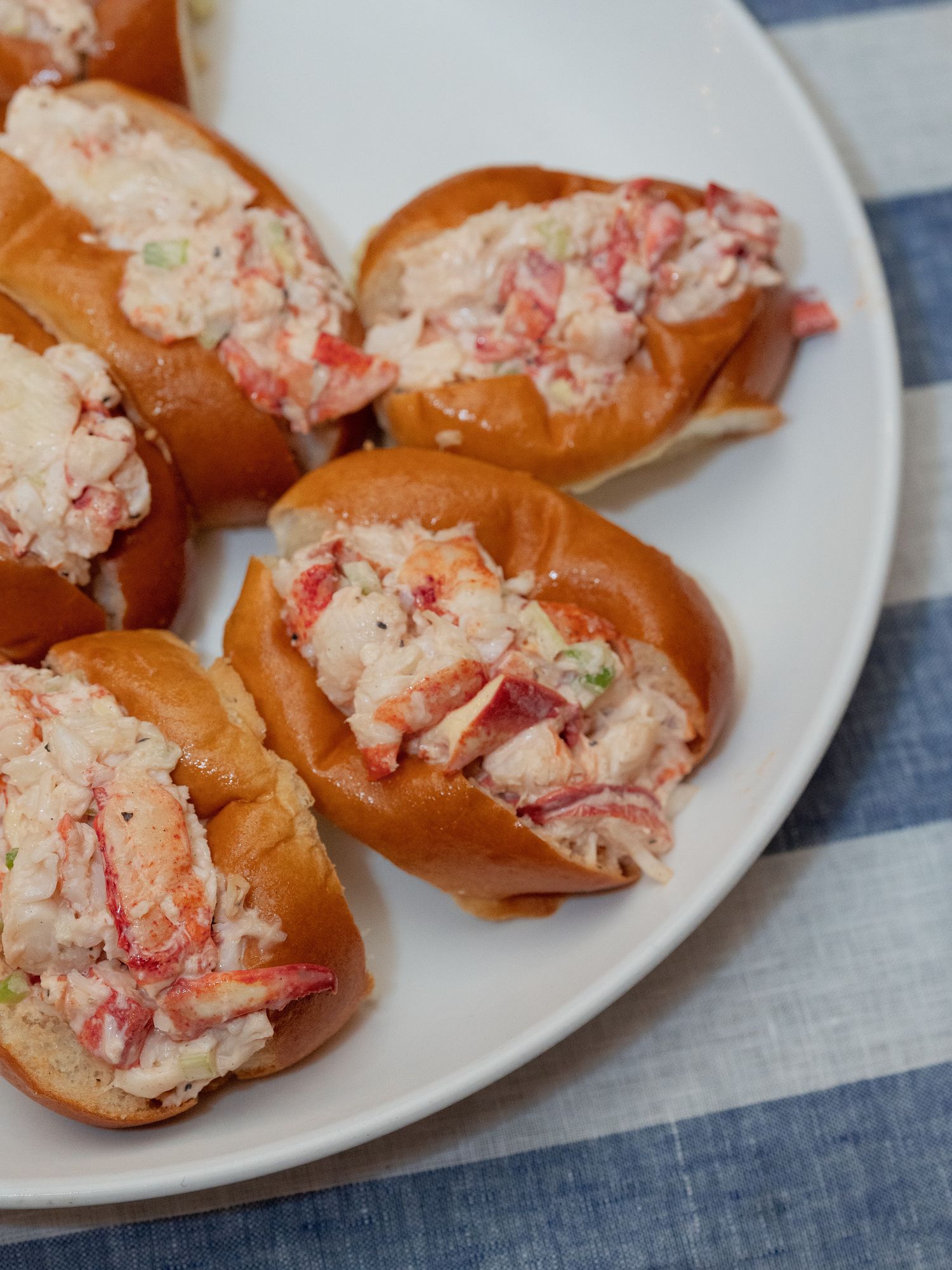 Mini lobster rolls served on toasted brioche buns on a white plate with blue striped linen.