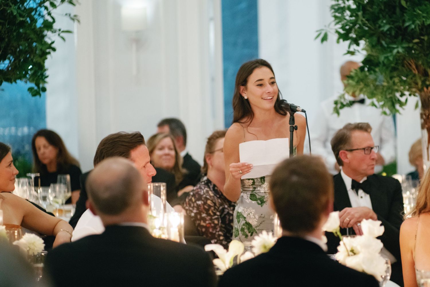 Bride in strapless gown delivering a heartfelt speech at an elegantly decorated wedding reception table.
