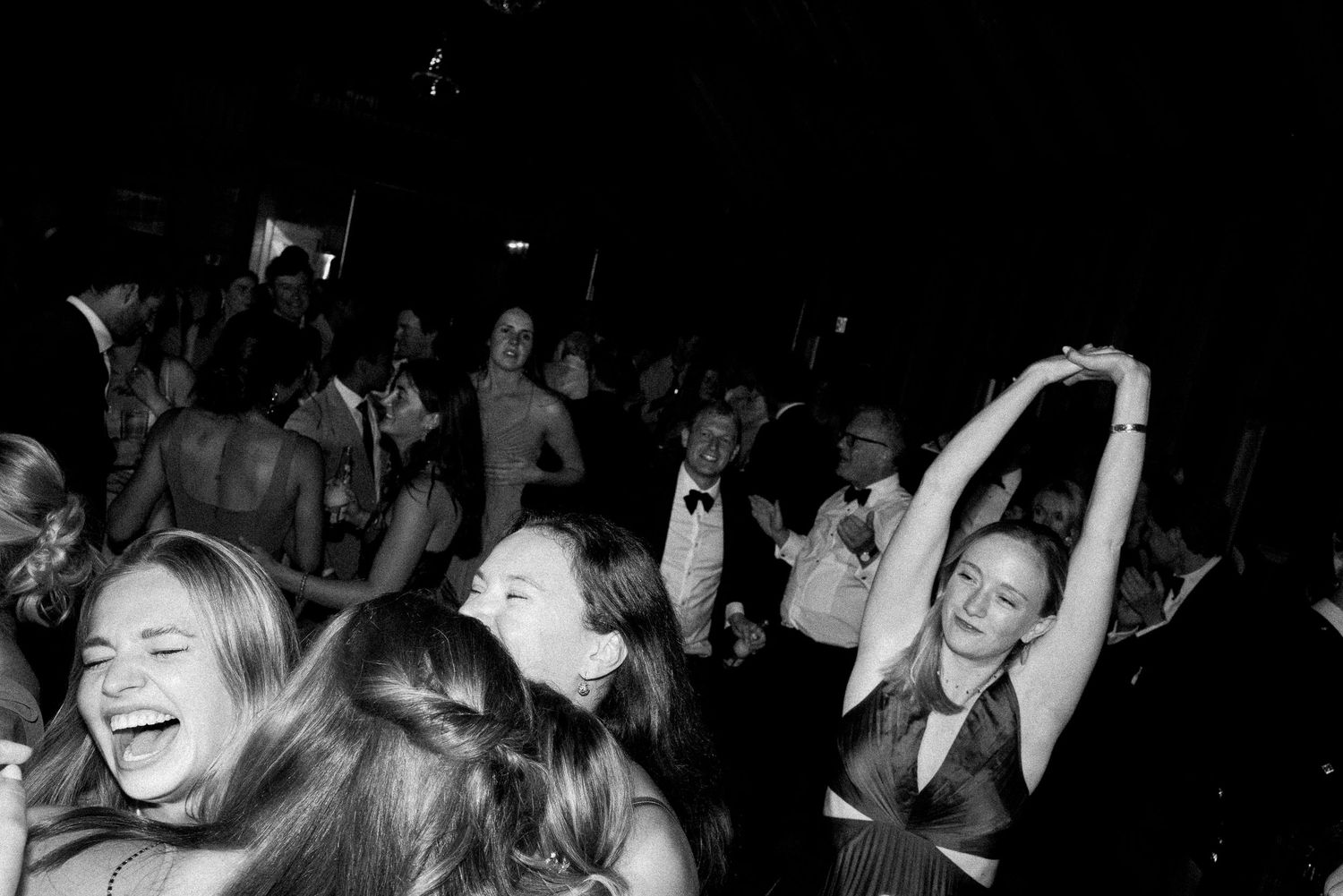 Black and white photo of joyful guests dancing and laughing at a formal evening event or wedding reception.