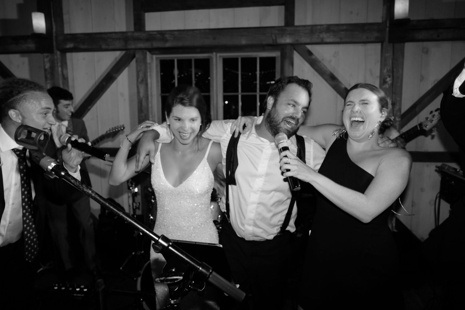 Bride and groom sing joyfully with live band at rustic barn wedding reception.