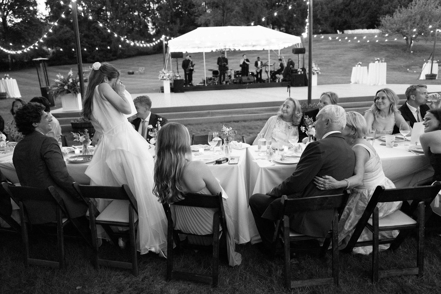 Black and white photo of bride giving a speech at an elegant outdoor wedding reception dinner.