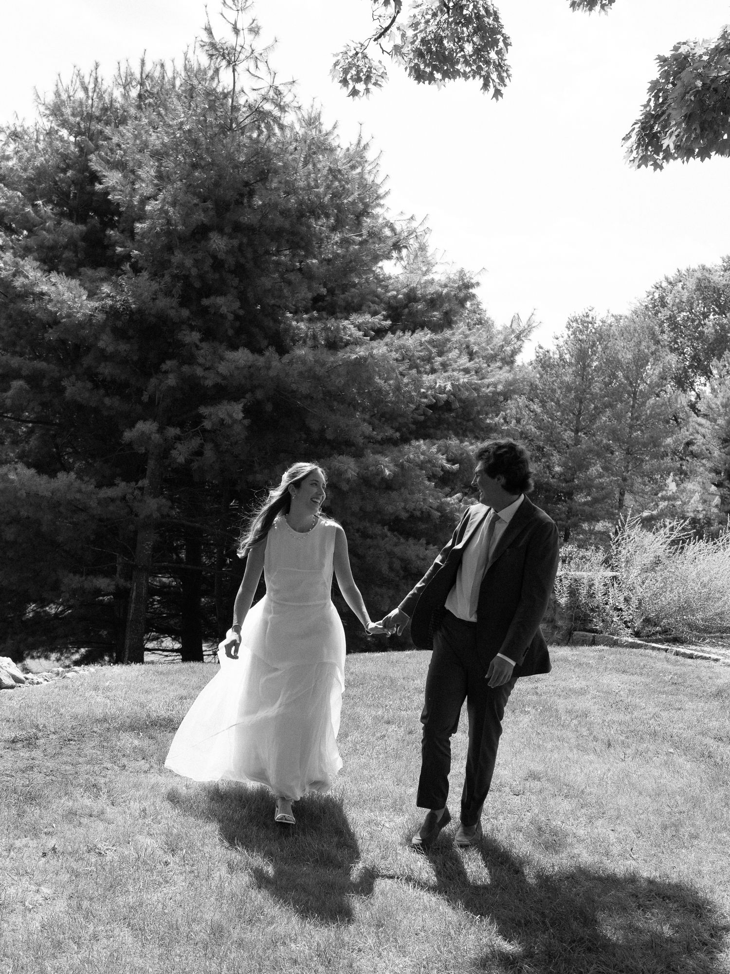 Black and white photo of newlyweds holding hands and walking across a green lawn at their wedding.
