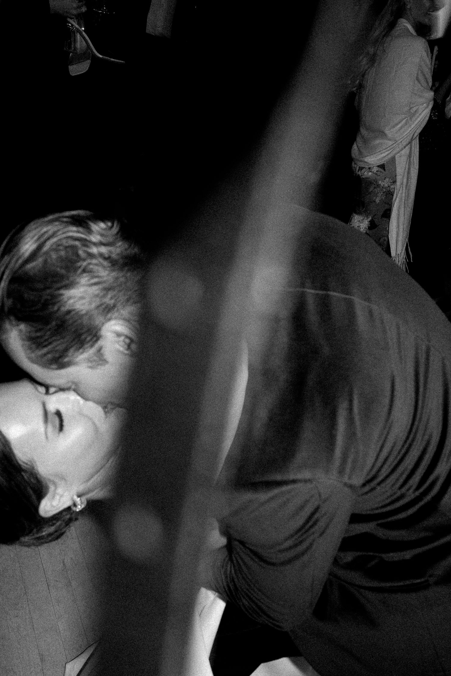 Black and white photo of a couple sharing a romantic kiss on a dimly lit dance floor.