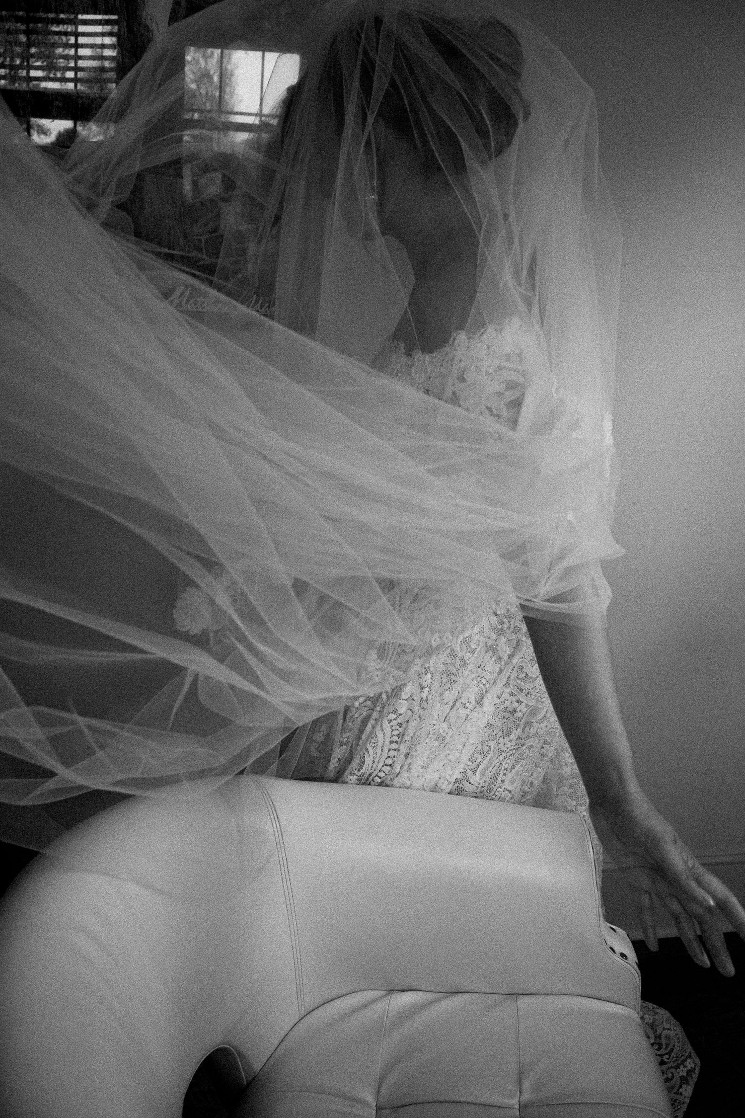 Black and white photo of a bride in a lace wedding dress, her flowing veil dramatically billowing around her.