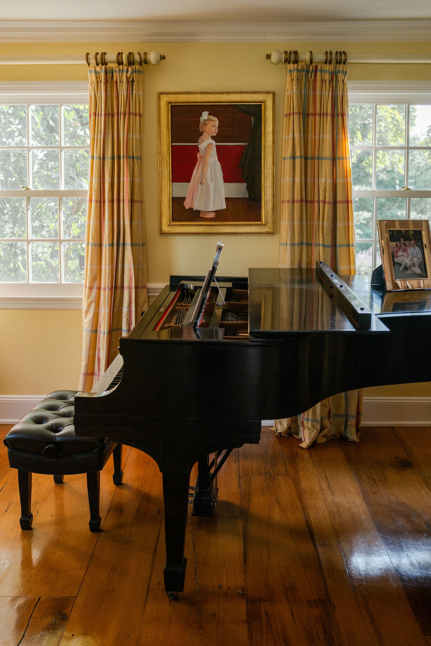 Elegant grand piano in a sunlit room with hardwood floors and a portrait painting on the wall.