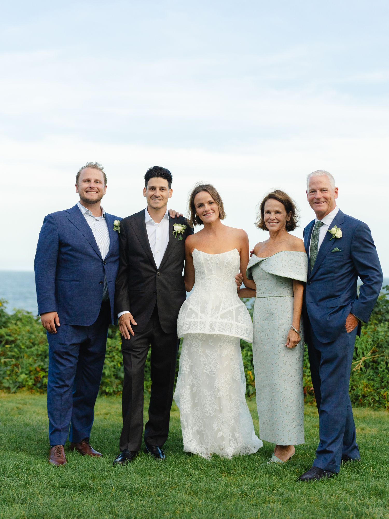 Wedding couple posing with family members outdoors with ocean view background.