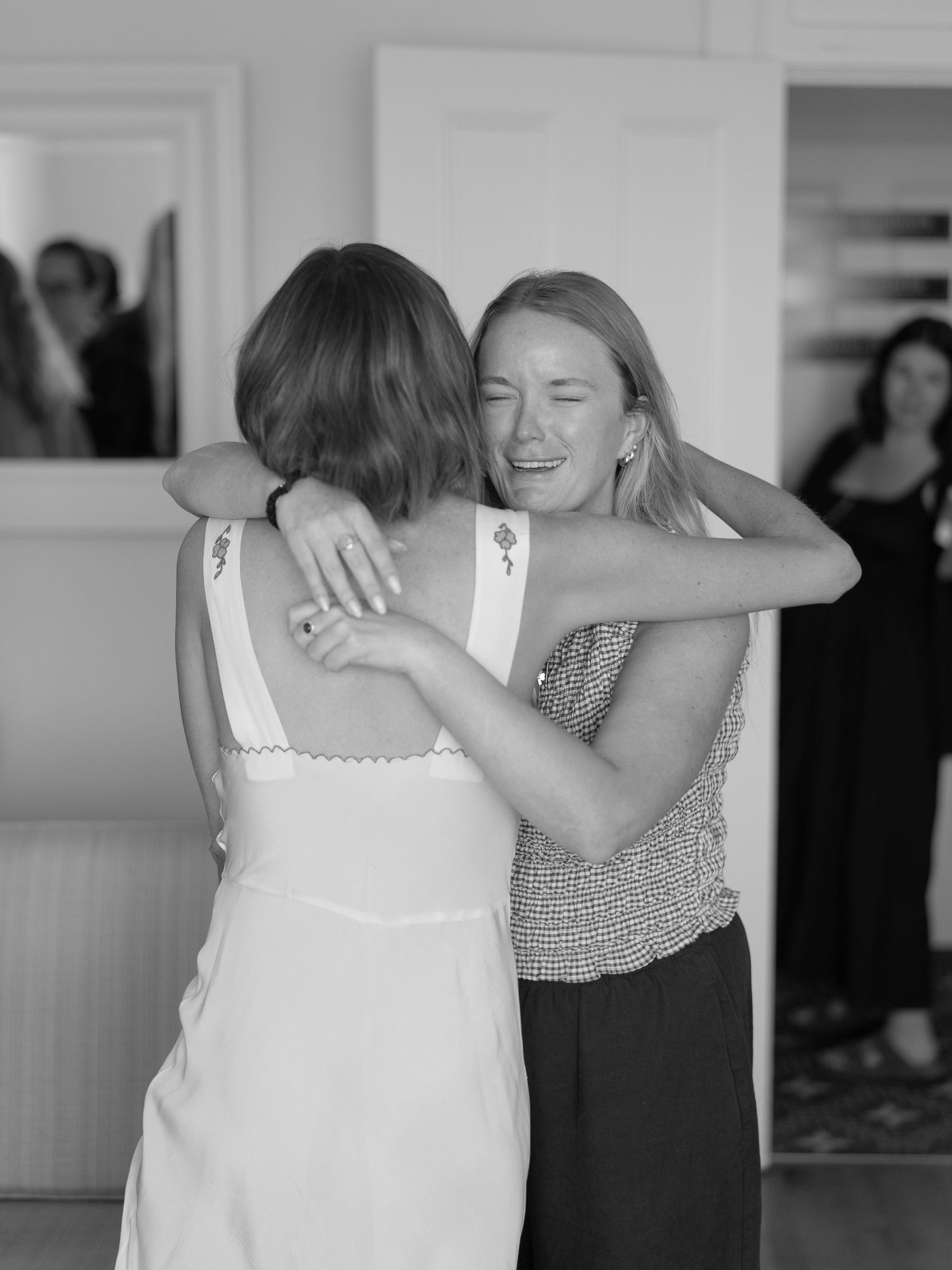 Black and white photo of two women sharing an emotional hug at a wedding celebration.
