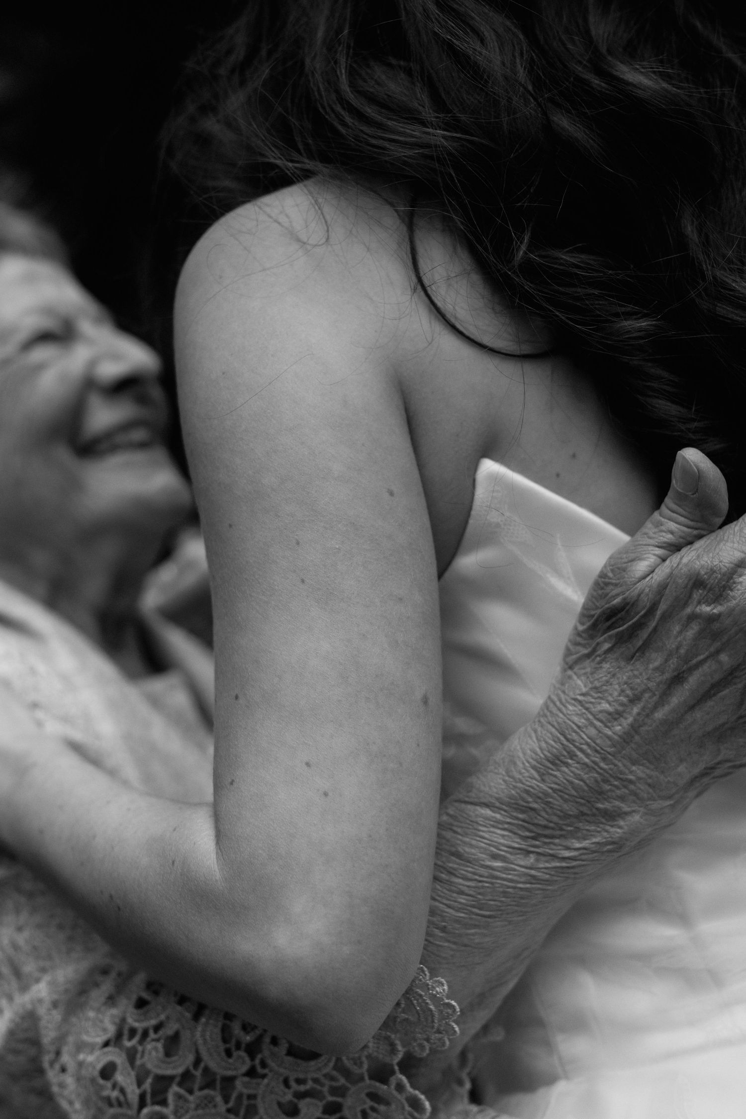 Black and white photo of an elderly woman embracing a young bride in a strapless wedding gown.