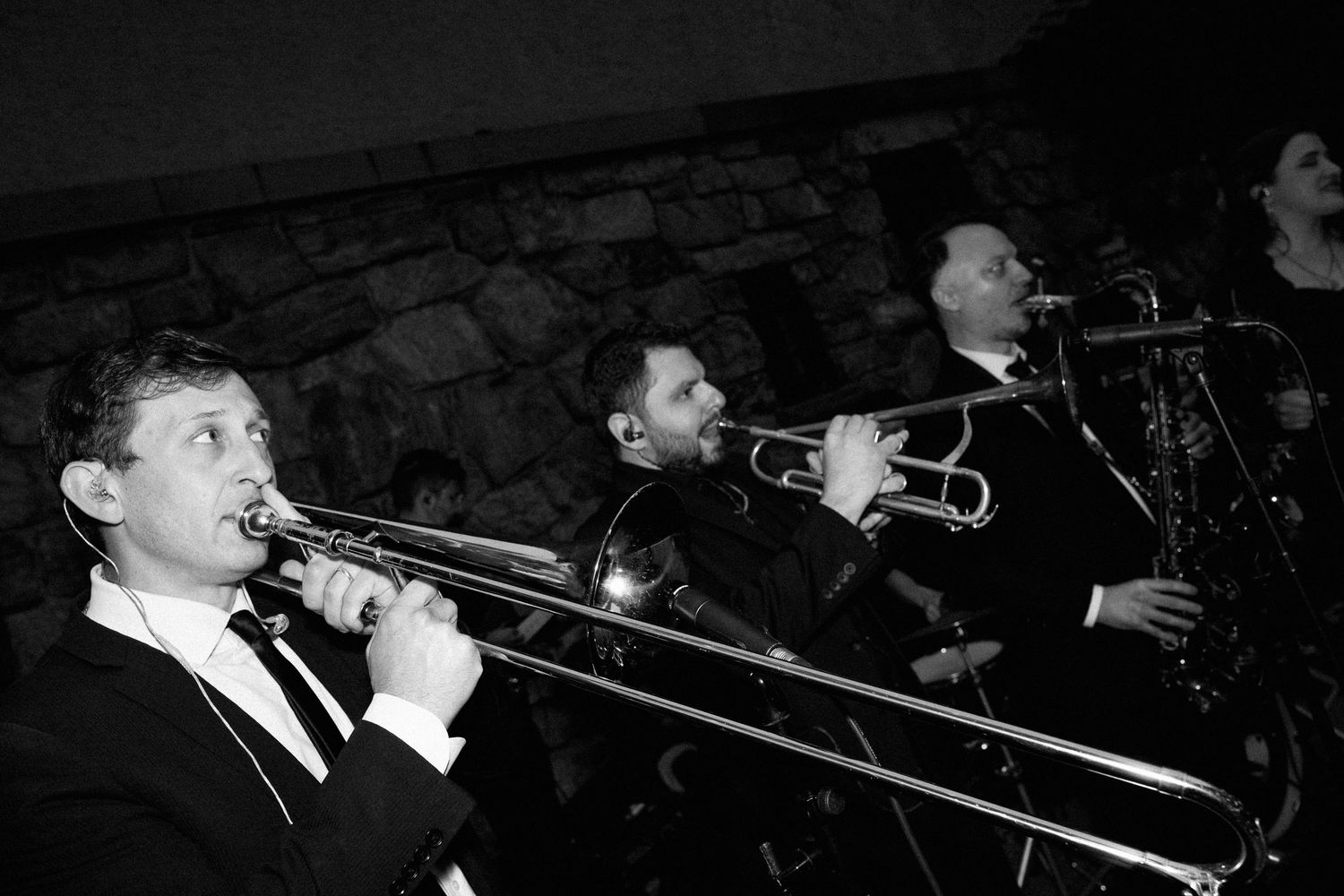Black and white photo of a live jazz band playing trombone and saxophone at a wedding reception.