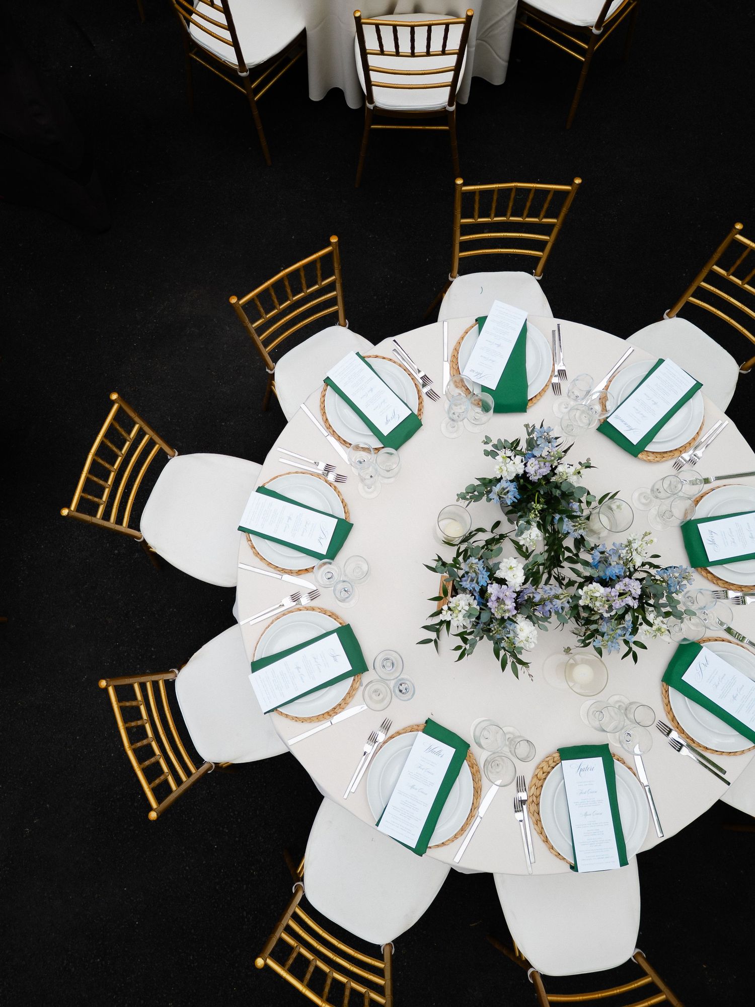 Aerial view of elegant wedding reception table with gold chiavari chairs, green napkins, and floral centerpiece.