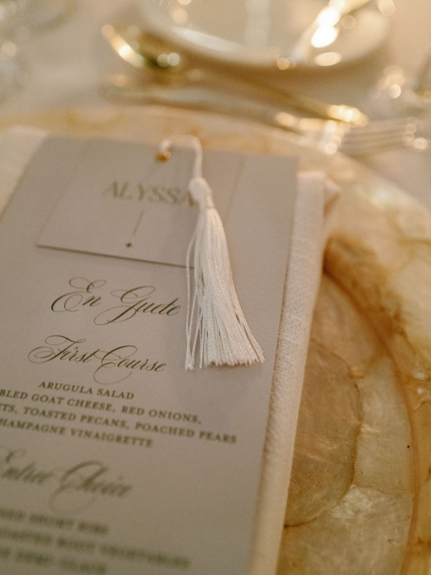 Close-up of elegant wedding menu card with white tassel on gold charger plate.