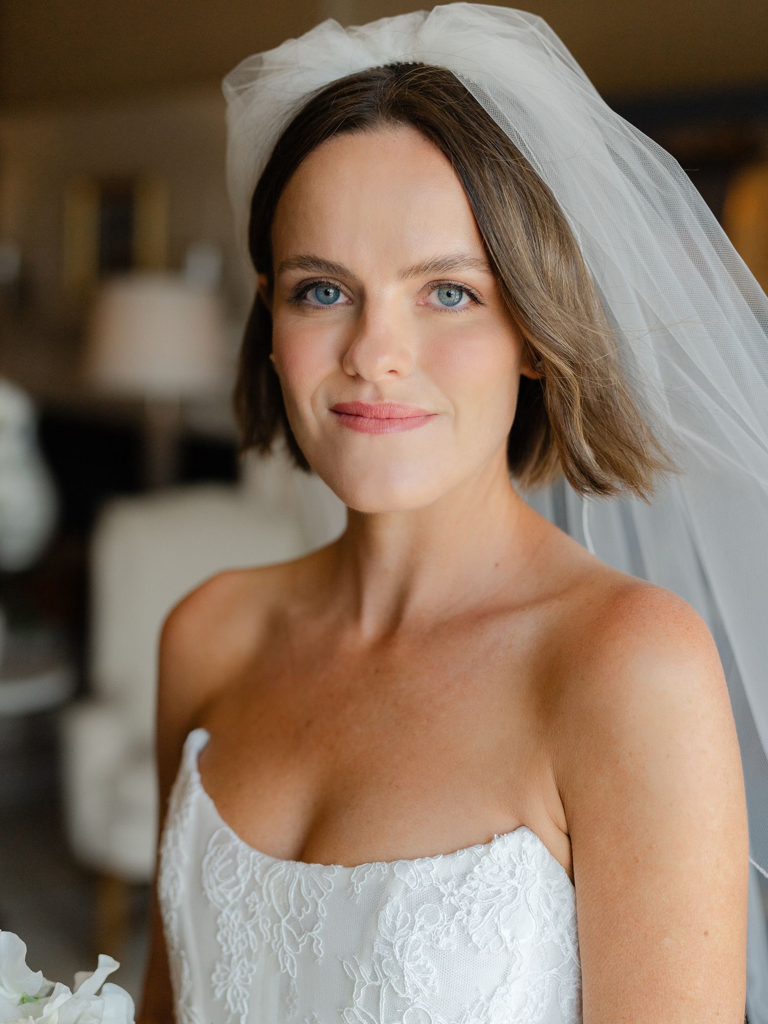 Close-up portrait of bride with short brown hair and blue eyes in strapless lace gown.