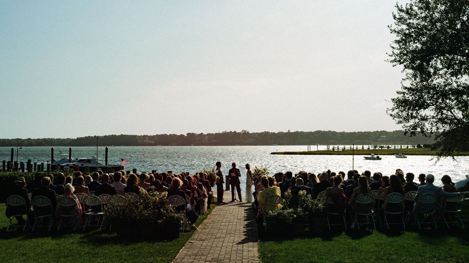 Waterfront wedding ceremony with guests seated outdoors overlooking a serene lake.